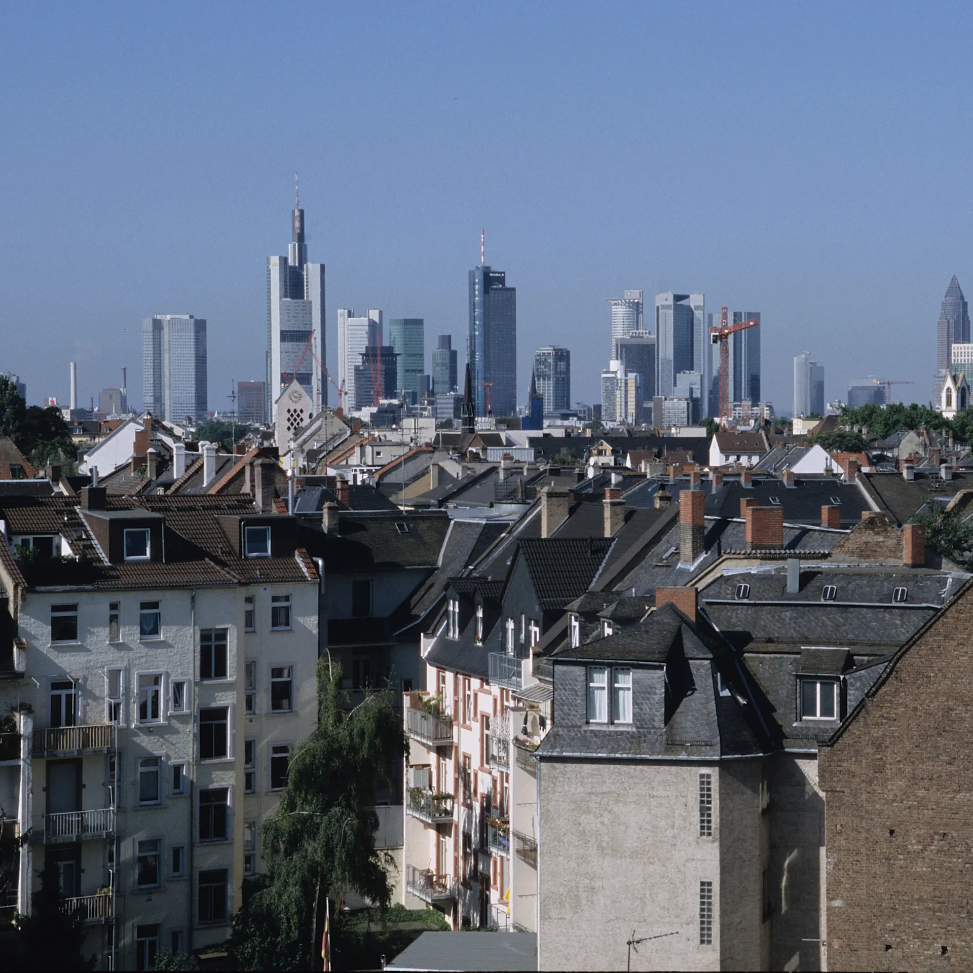 Blick über Wohnhäuser mit moderner Skyline im Hintergrund bei klarem Himmel.