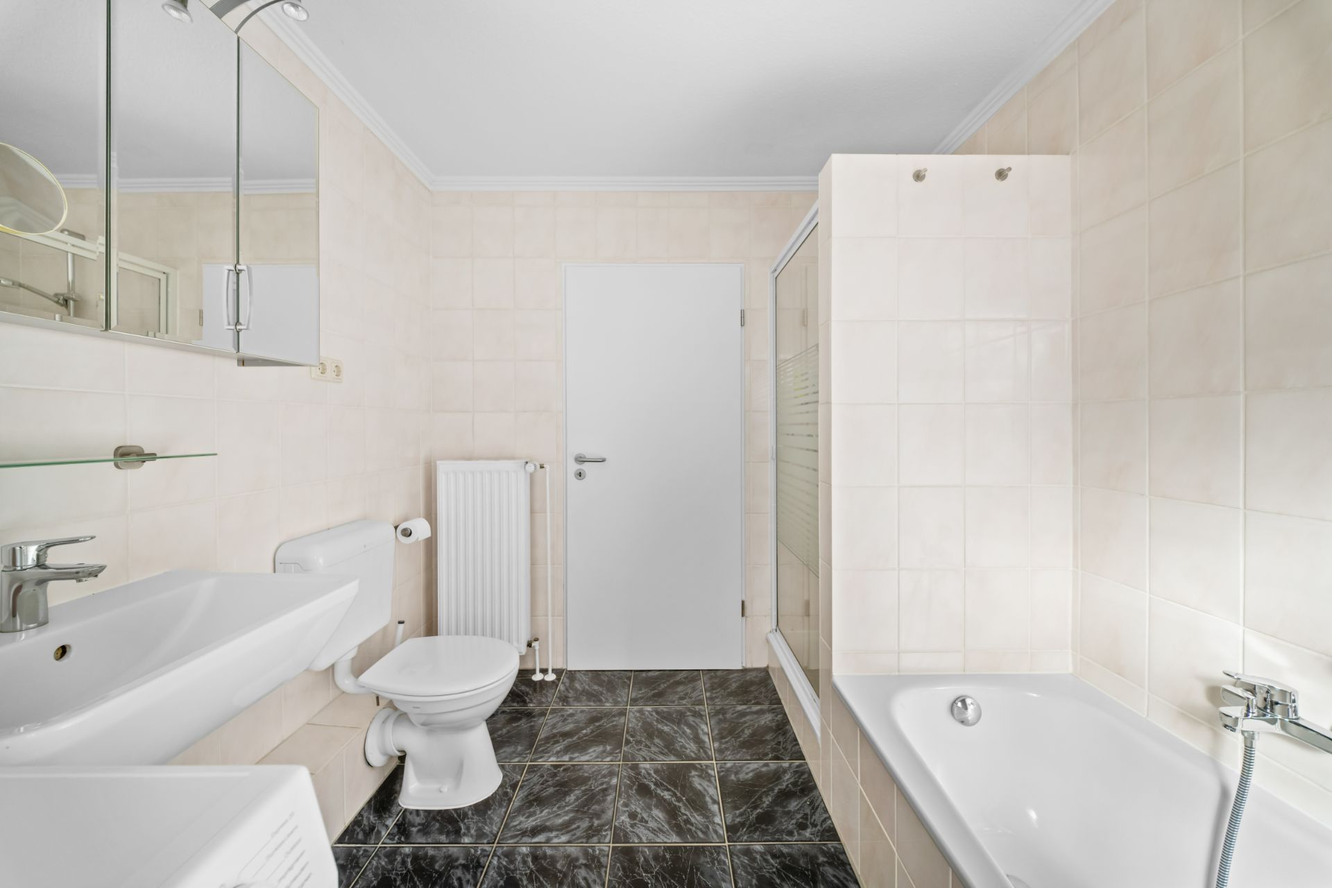 Helles Badezimmer mit Waschbecken, Toilette, Dusche, Badewanne und dunklem Fliesenboden.