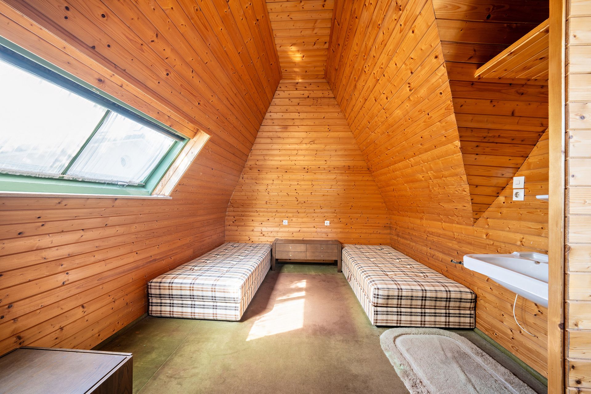 Dachzimmer mit Holzverkleidung, zwei Einzelbetten, Fenster und Waschbecken.