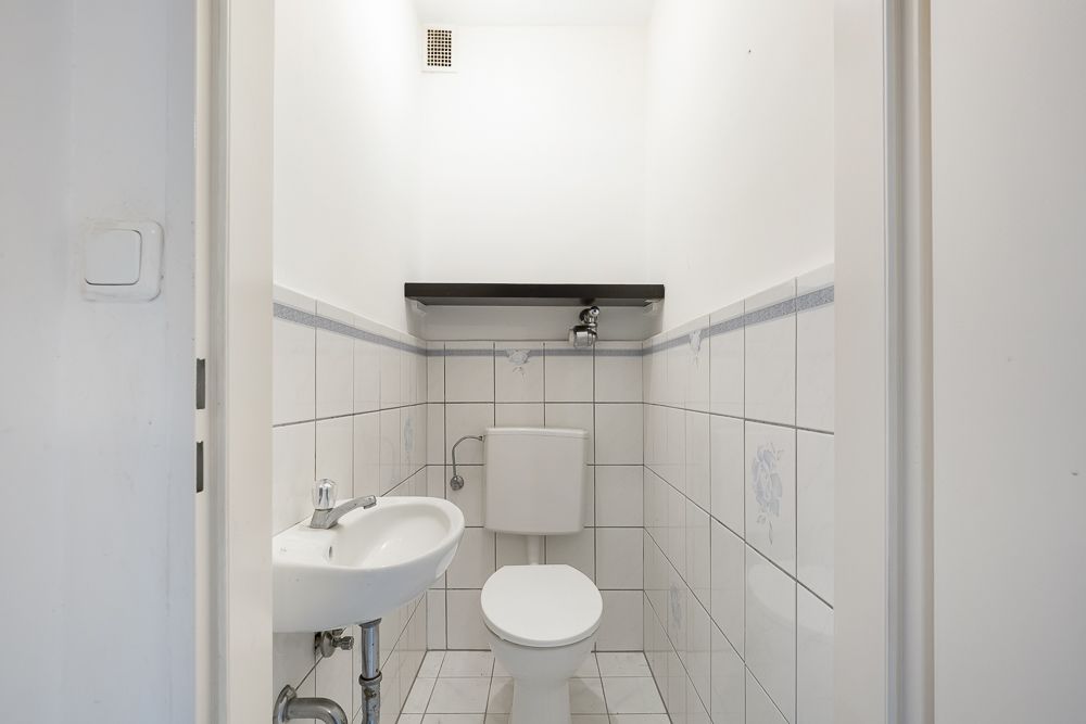 Kleines, weiß gefliestes WC mit Waschbecken und Ablage über der Toilette.