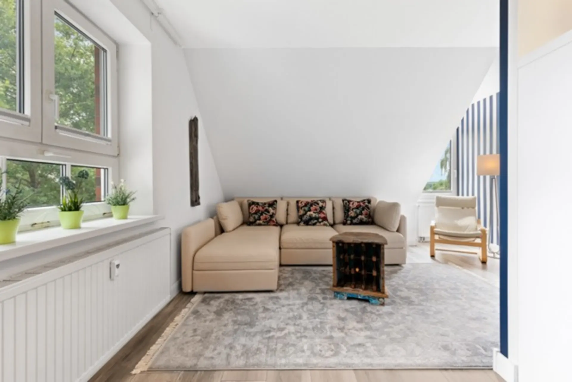 Helles Wohnzimmer mit Ecksofa, Teppich, Couchtisch und Pflanzen auf der Fensterbank.