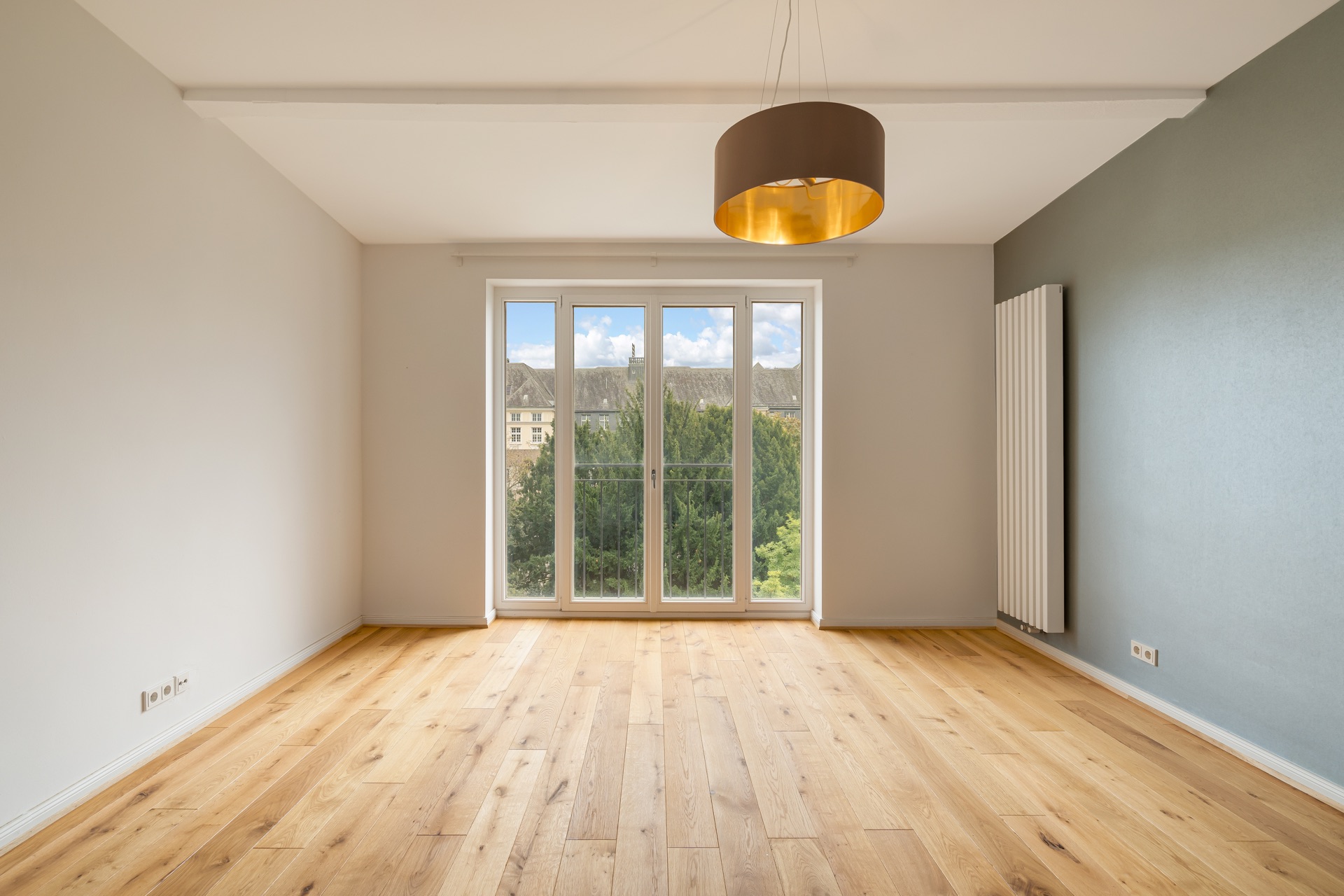 Leerer Raum mit Holzfußboden, großen Fenstern und moderner Deckenlampe.