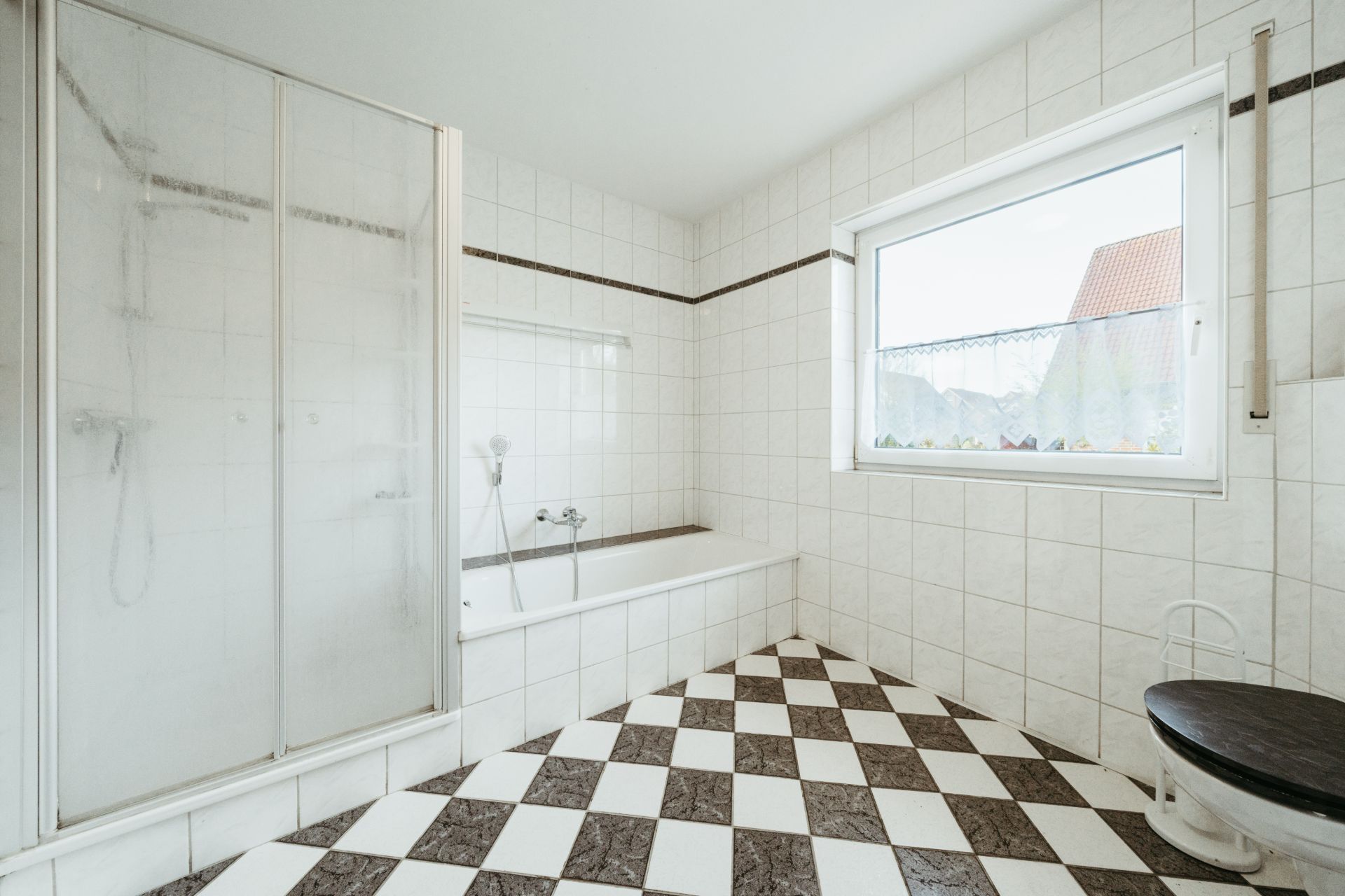 Helles Bad mit Dusche, Badewanne, Fenster und Schachbrettfliesenboden.