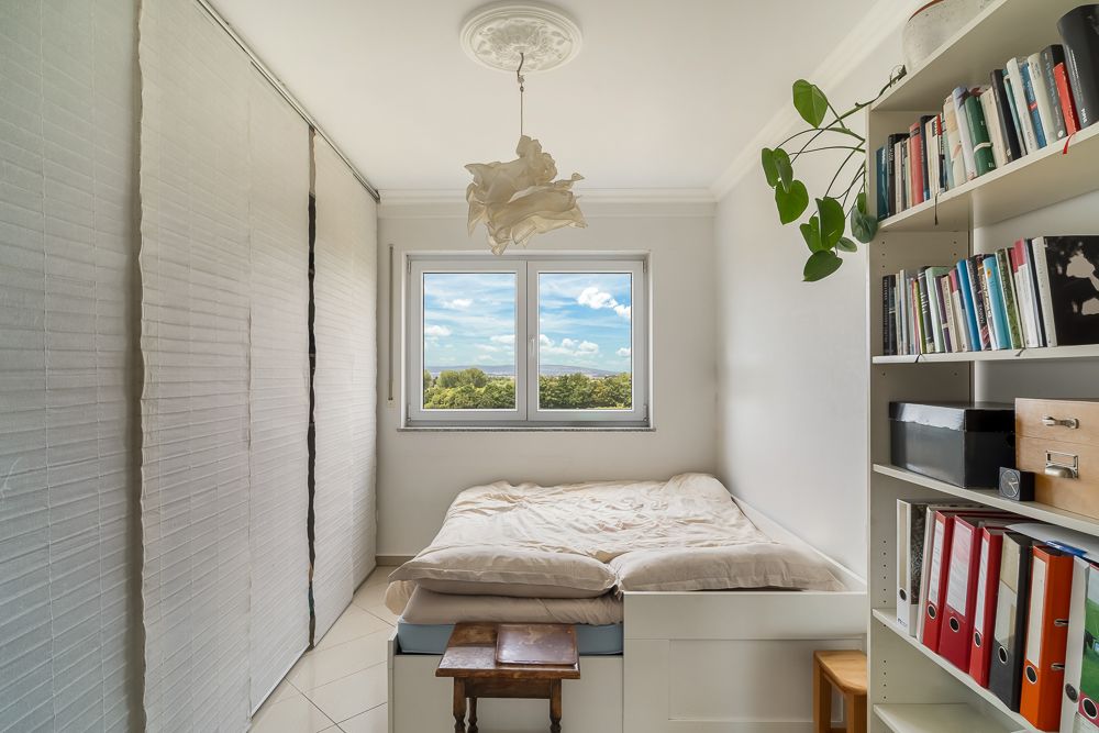 Kleines Schlafzimmer mit Bett, Bücherregal, Fenster und geschlossener Schrankwand.