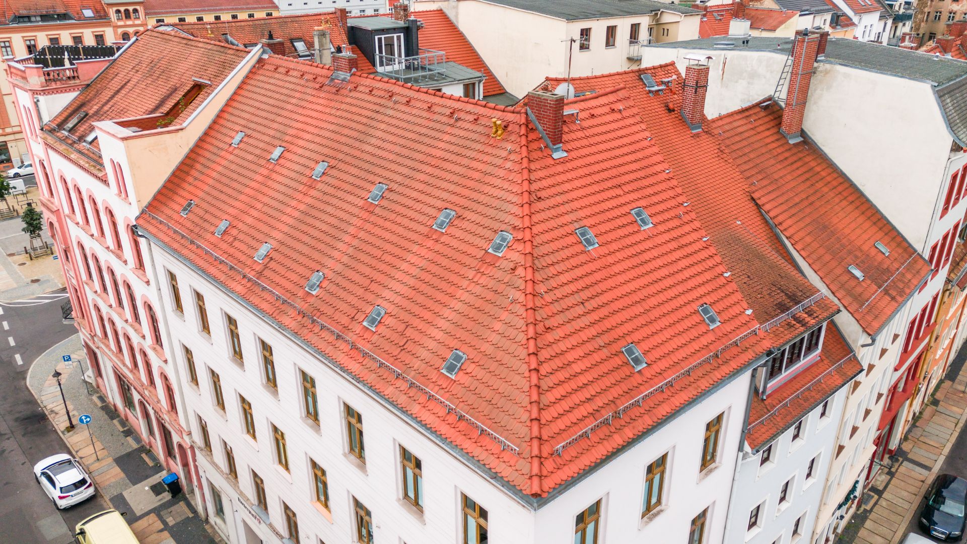 Großes Wohngebäude mit rotem Ziegeldach und vielen Dachfenstern, Blick von oben.