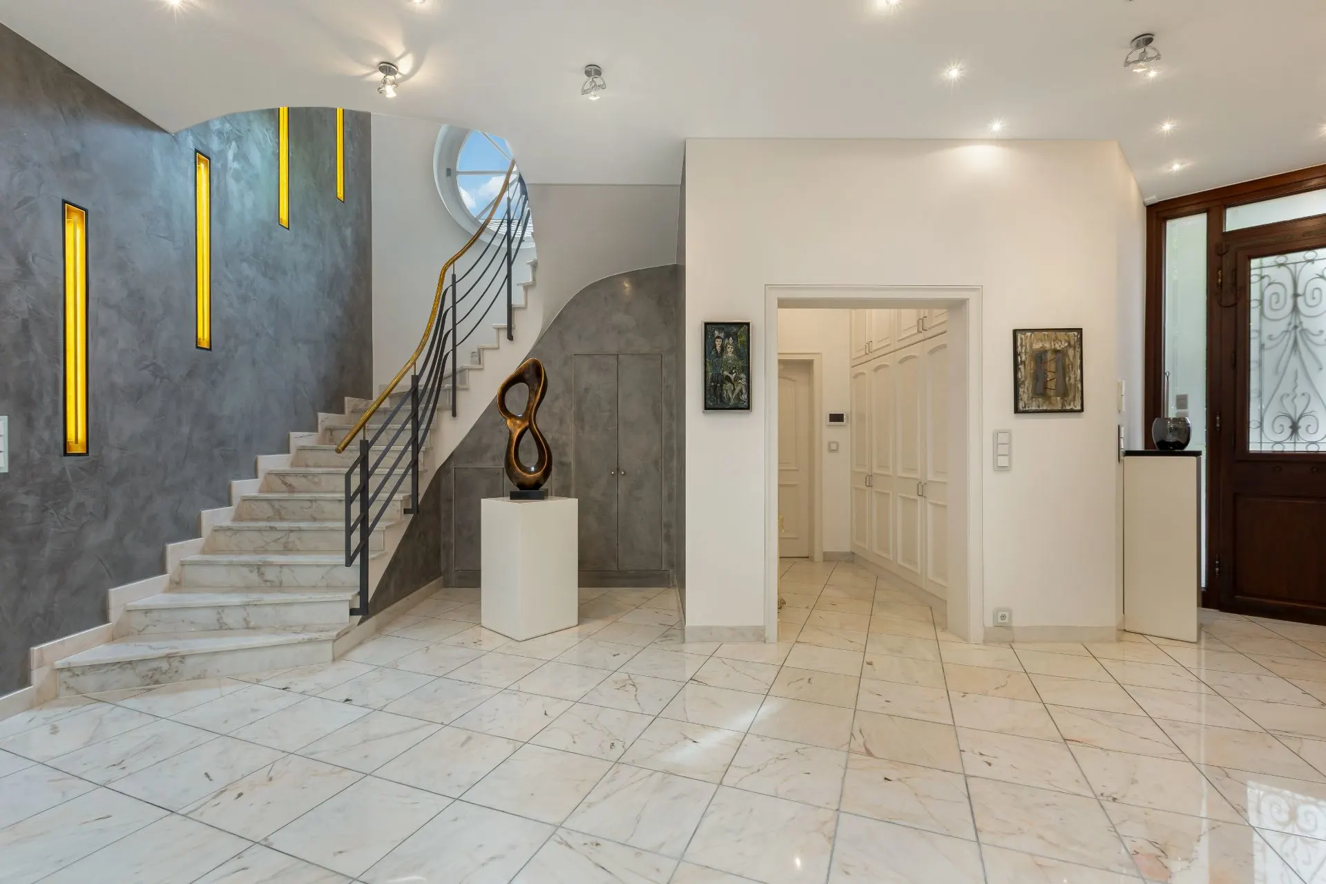 Heller Flur mit Marmorboden, Treppe, moderner Skulptur und Wandbeleuchtung.