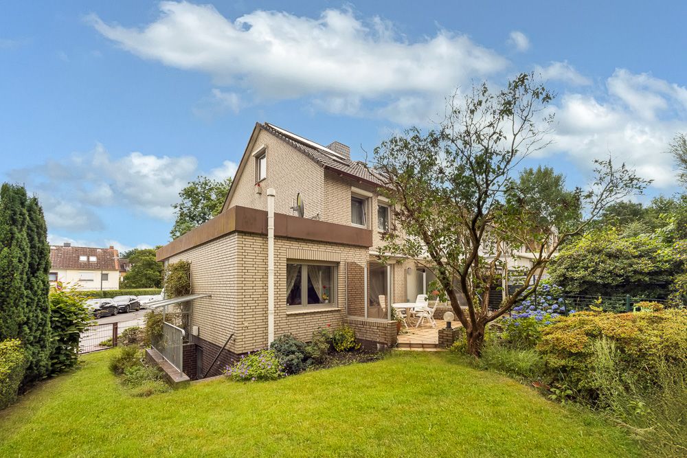 Modernes Einfamilienhaus mit Garten, Terrasse und Baum im Vordergrund.