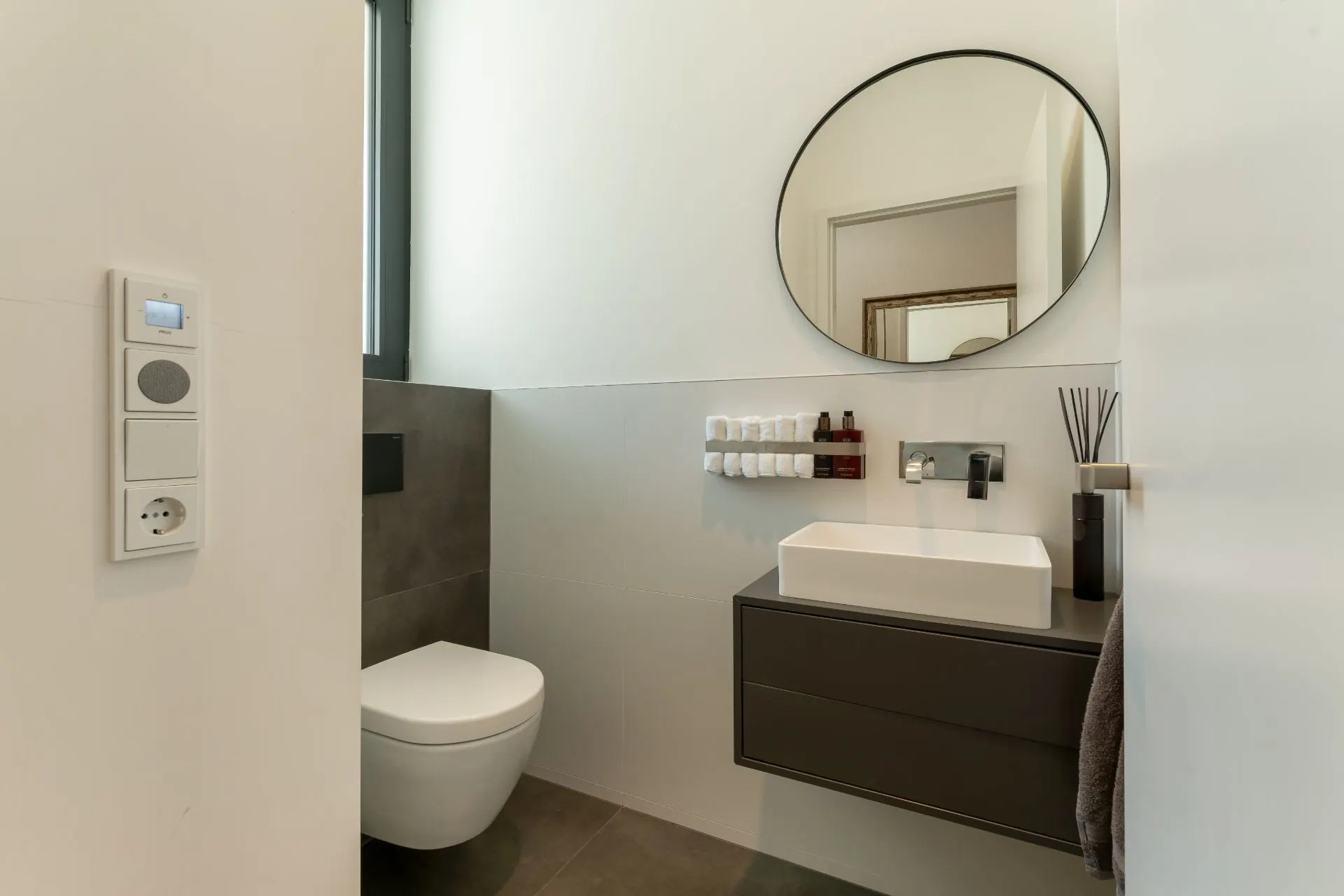 Modernes Badezimmer mit Wandspiegel, Waschbecken, WC und Ablage mit Pflegeprodukten.
