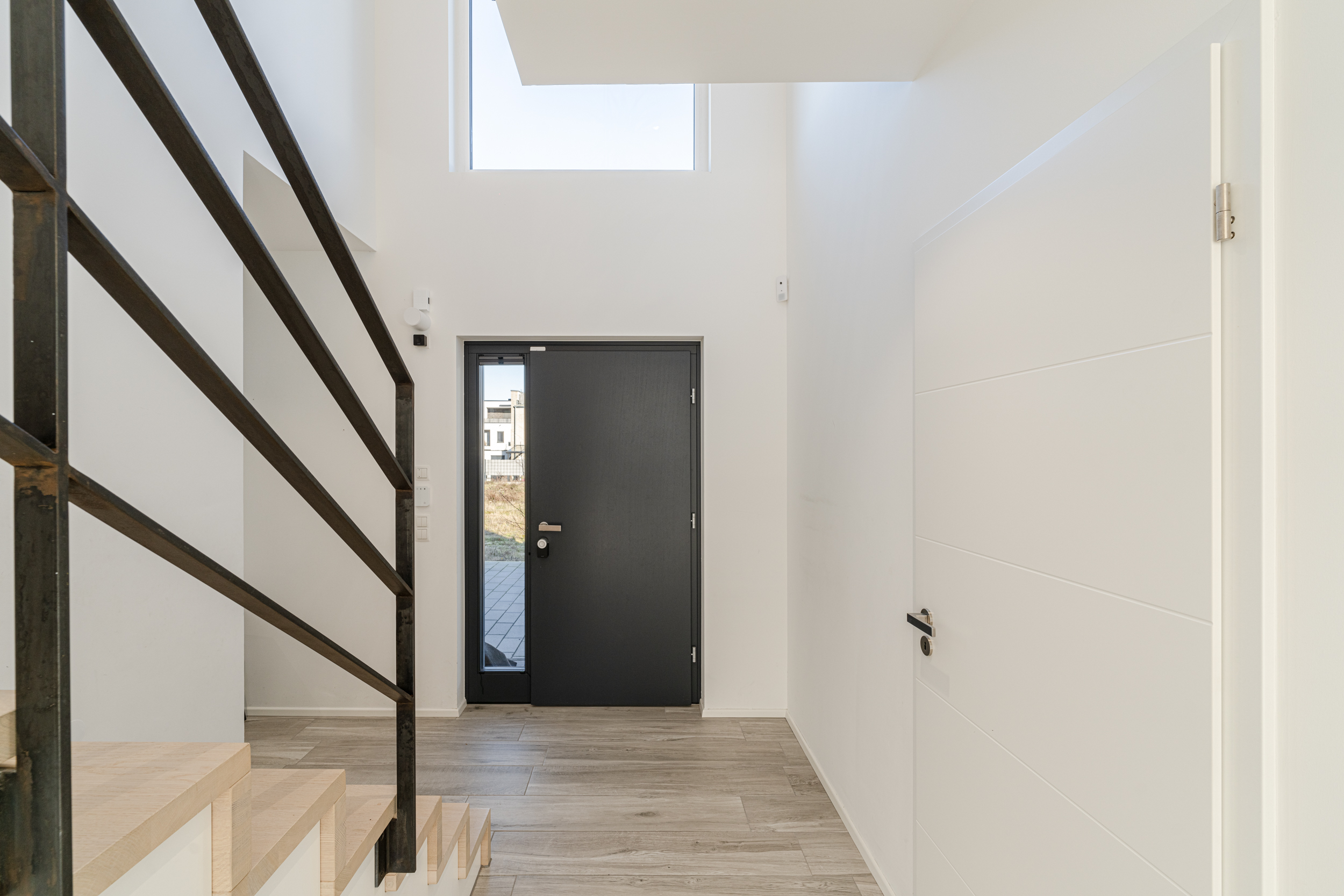 Heller Flur mit grauer Eingangstür, seitlicher Treppe und weißer Wand.