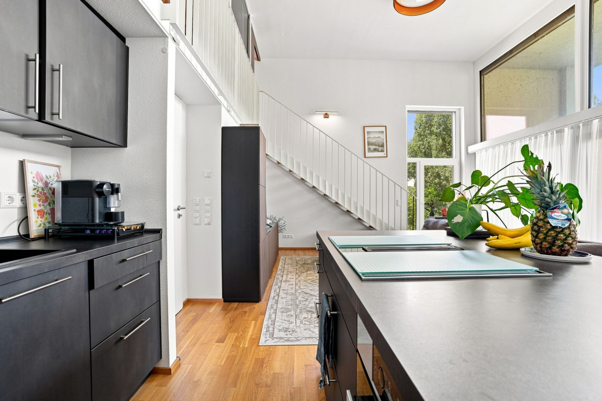 Moderne Küche mit dunklen Schränken, Holzboden und Treppe im Hintergrund.