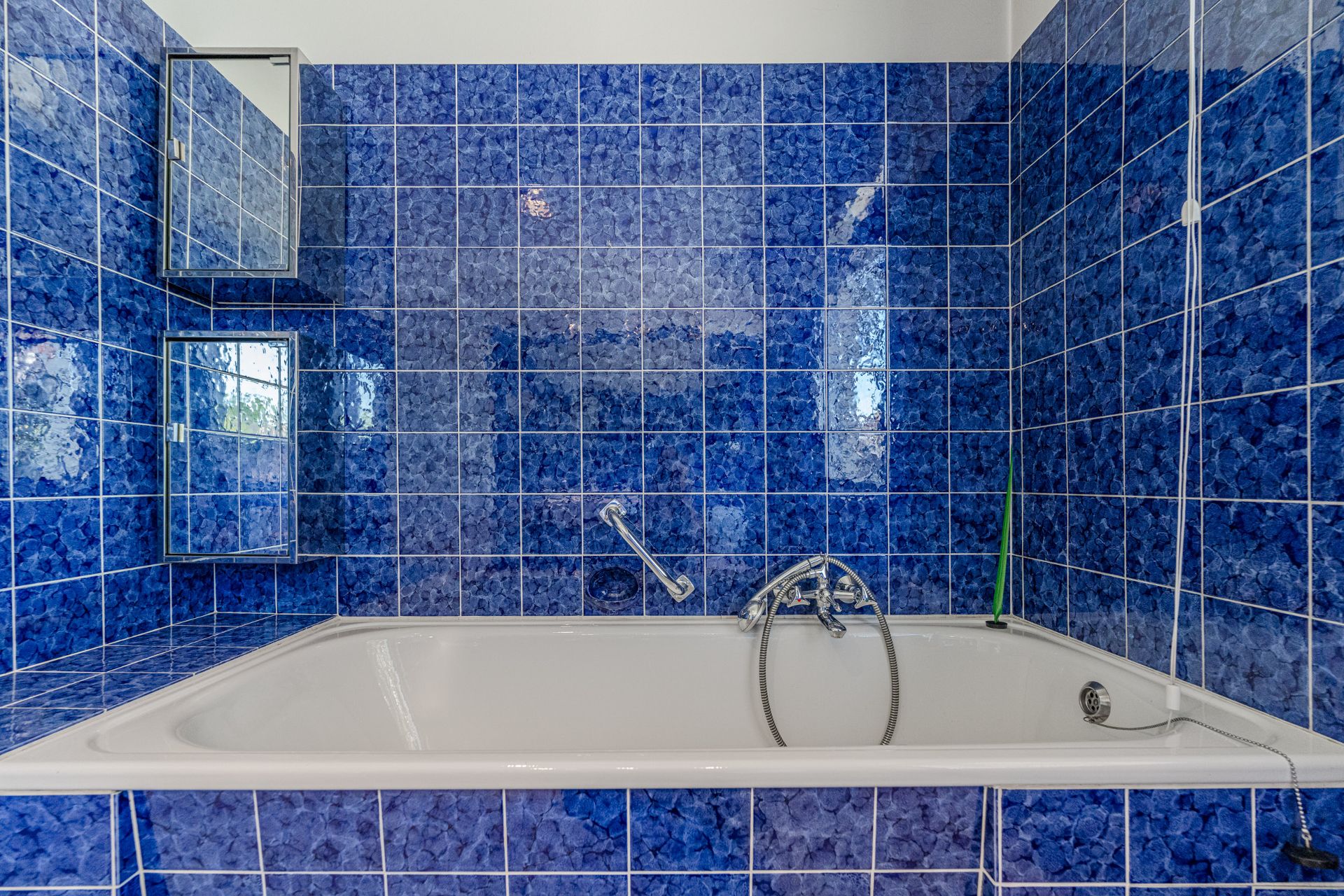 Badewanne mit blauen Fliesen an Wand und Seite, zwei Spiegelschränke an der Wand.