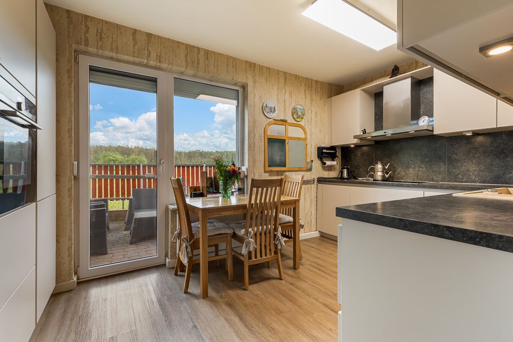 Moderne Wohnküche mit Esstisch, Stühlen und Zugang zur Terrasse mit Blick ins Grüne.