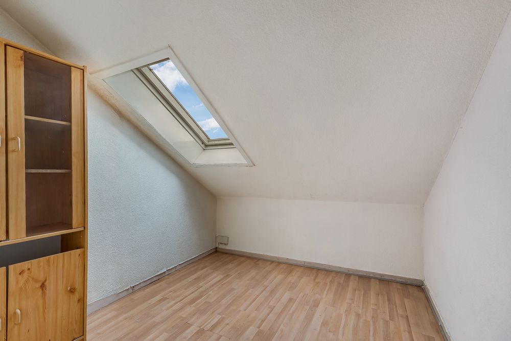 Leerer Raum mit Dachschrägen, Dachfenster und Holzschrank auf Laminatboden.