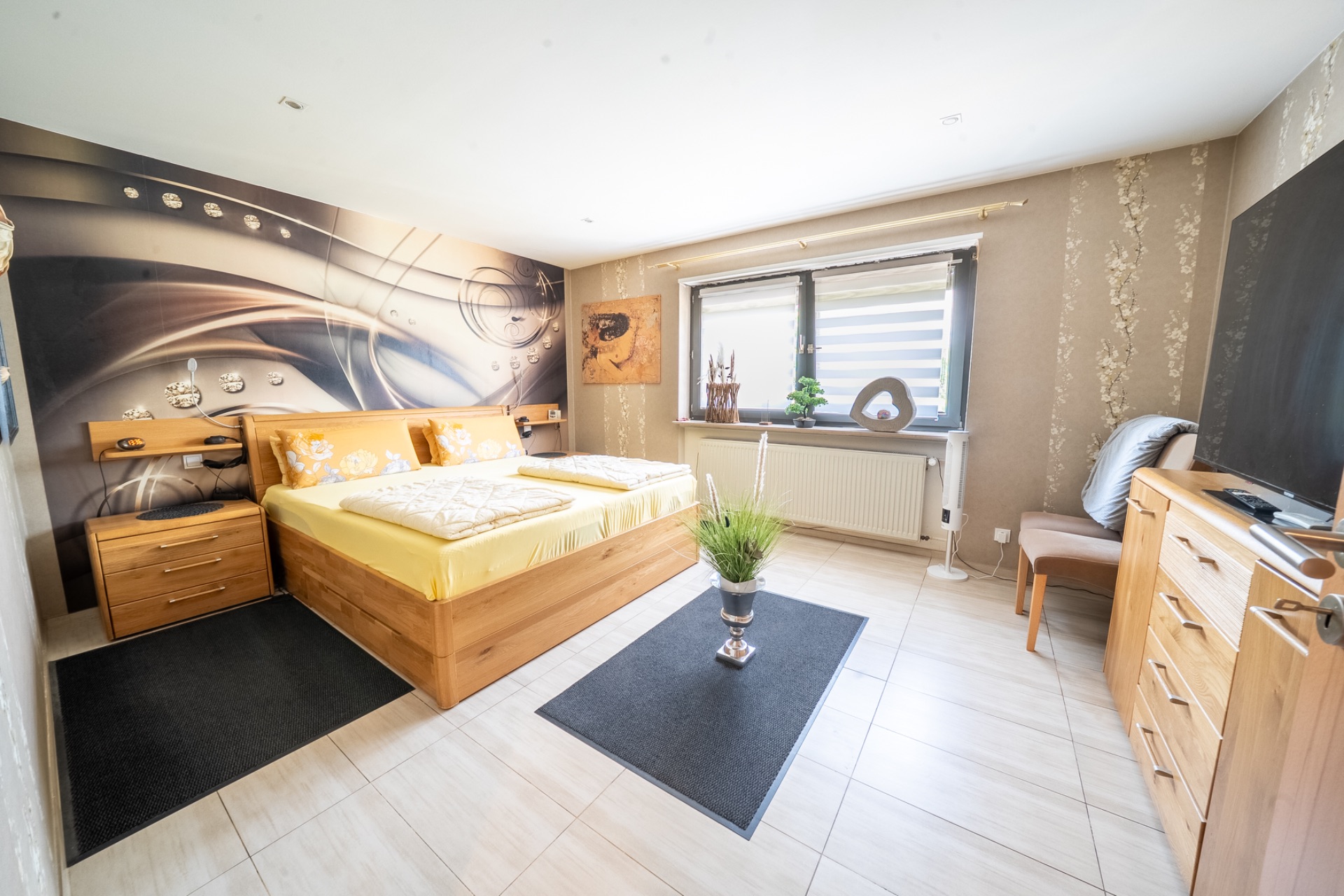 Modernes Schlafzimmer mit Doppelbett, Holzmöbeln, großem Fenster und Wanddekoration.