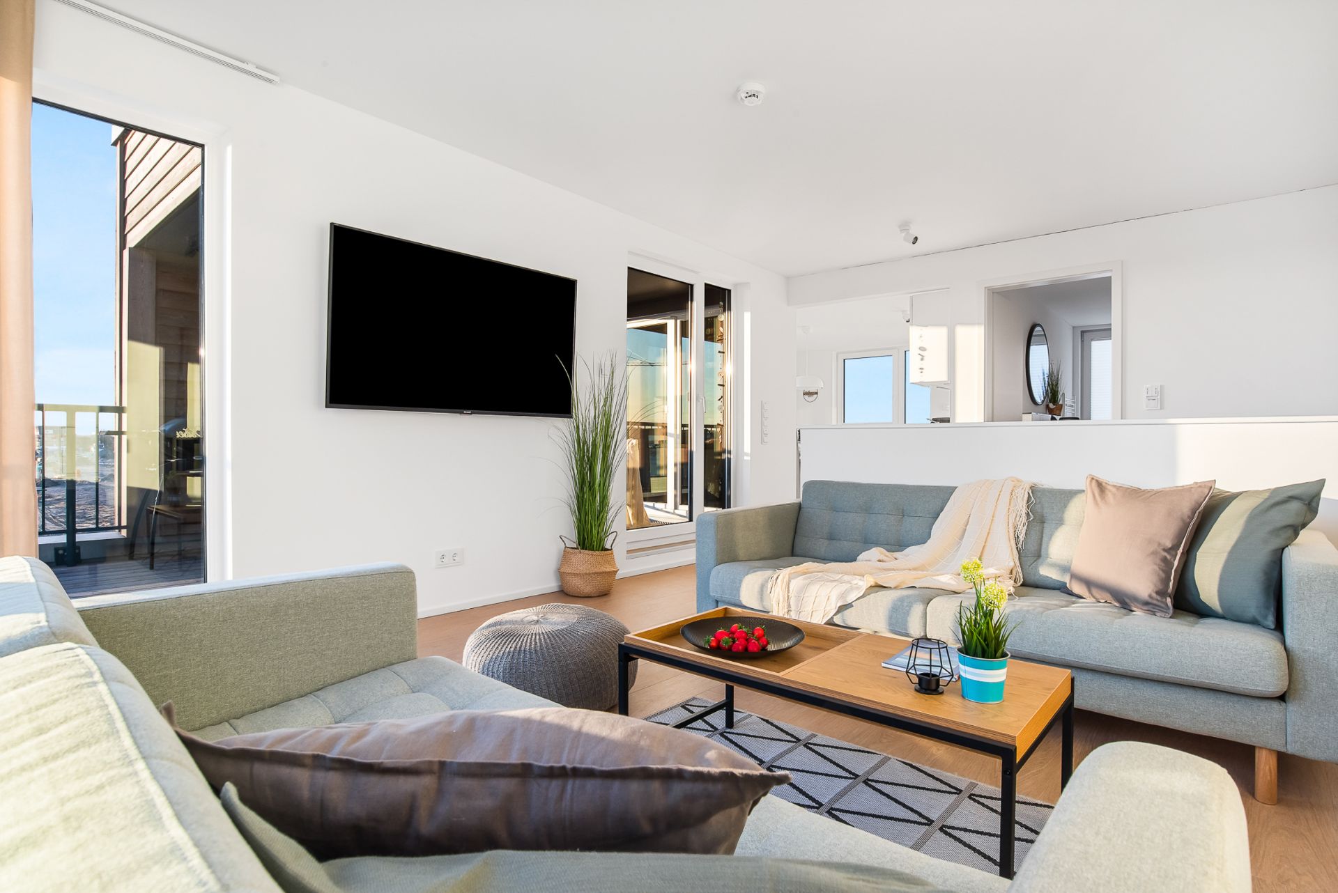 Modernes Wohnzimmer mit zwei Sofas, Couchtisch, Fernseher an der Wand und Zugang zum Balkon.