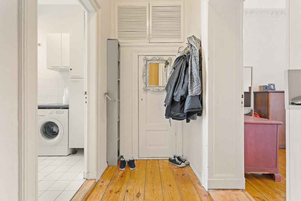 Flur mit Holzboden, Garderobe, Spiegel und Blick in Waschküche mit Waschmaschine.