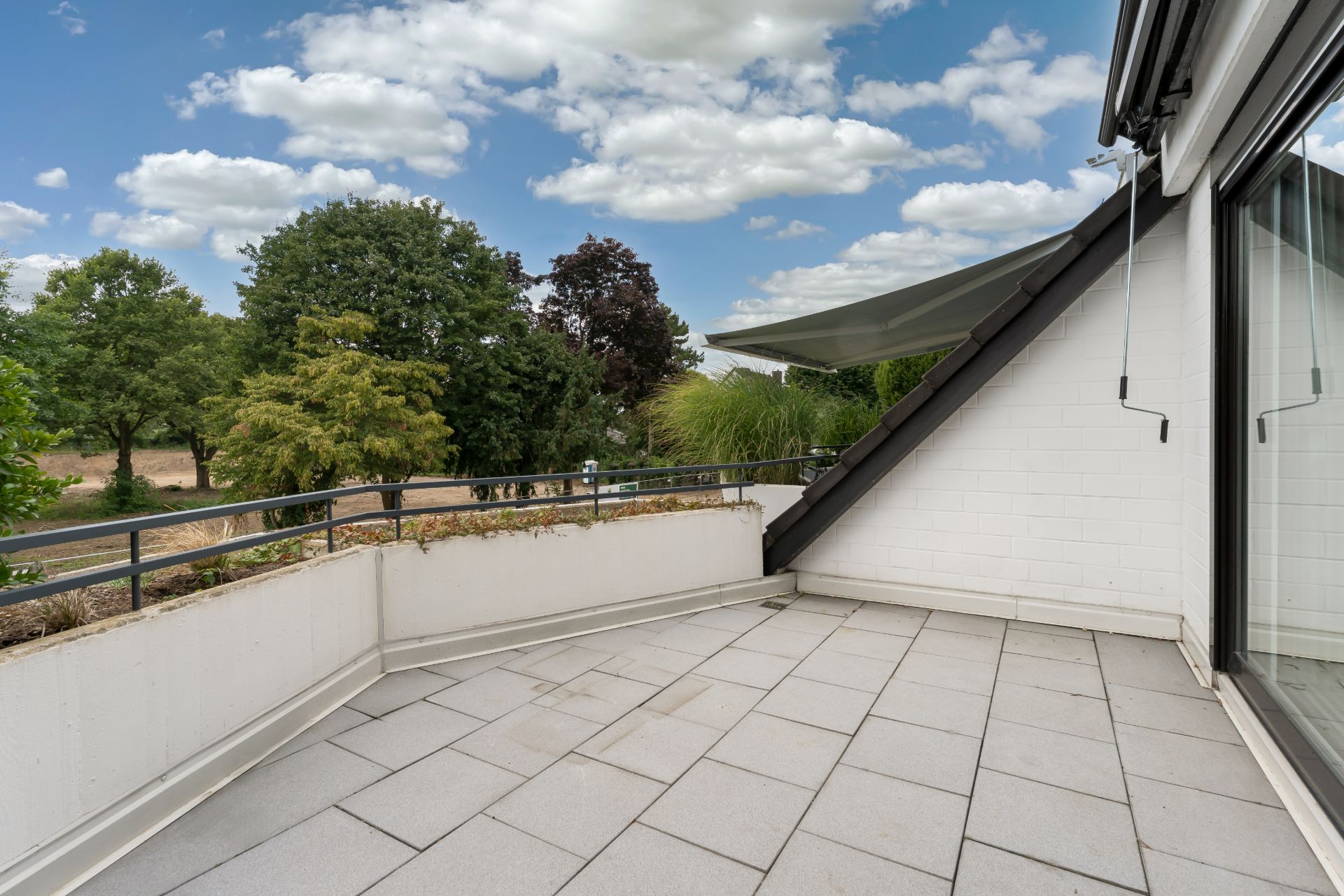 Geräumiger Balkon mit Fliesenboden, Geländer und Blick auf grüne Bäume.