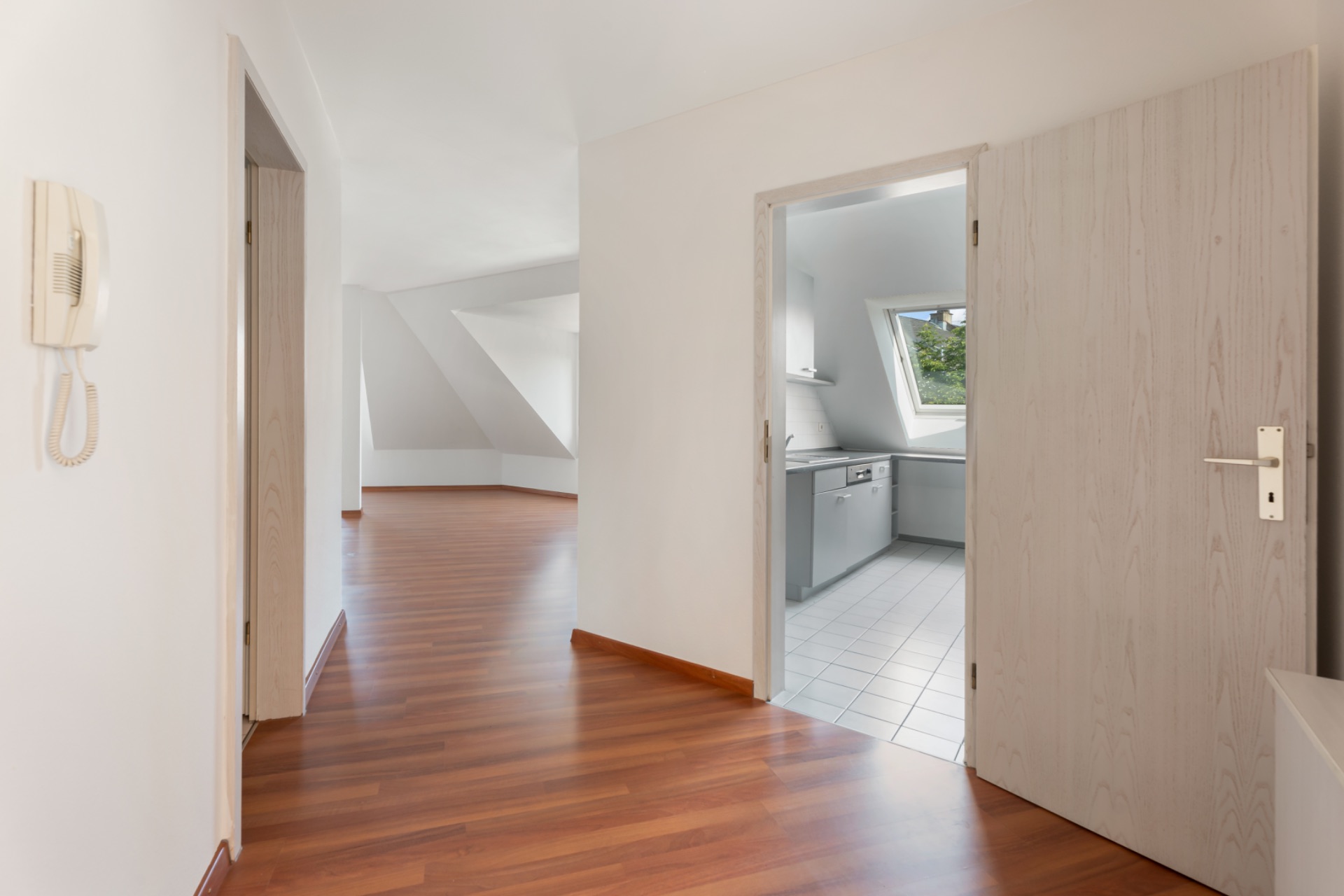 Heller Flur mit Holzboden, angrenzender Küche und großem Wohnraum mit Dachschräge.