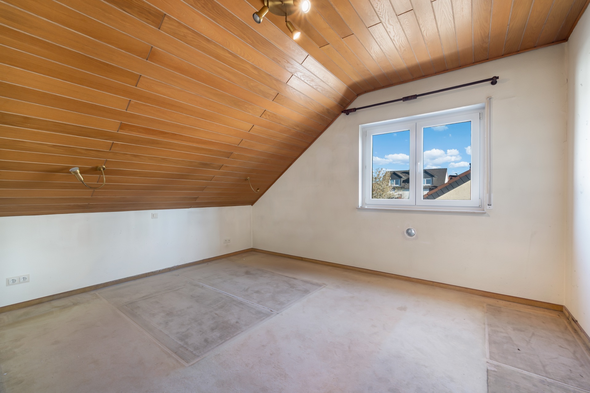 Leerer Dachraum mit Holzdecke, Fenster und Teppichboden.