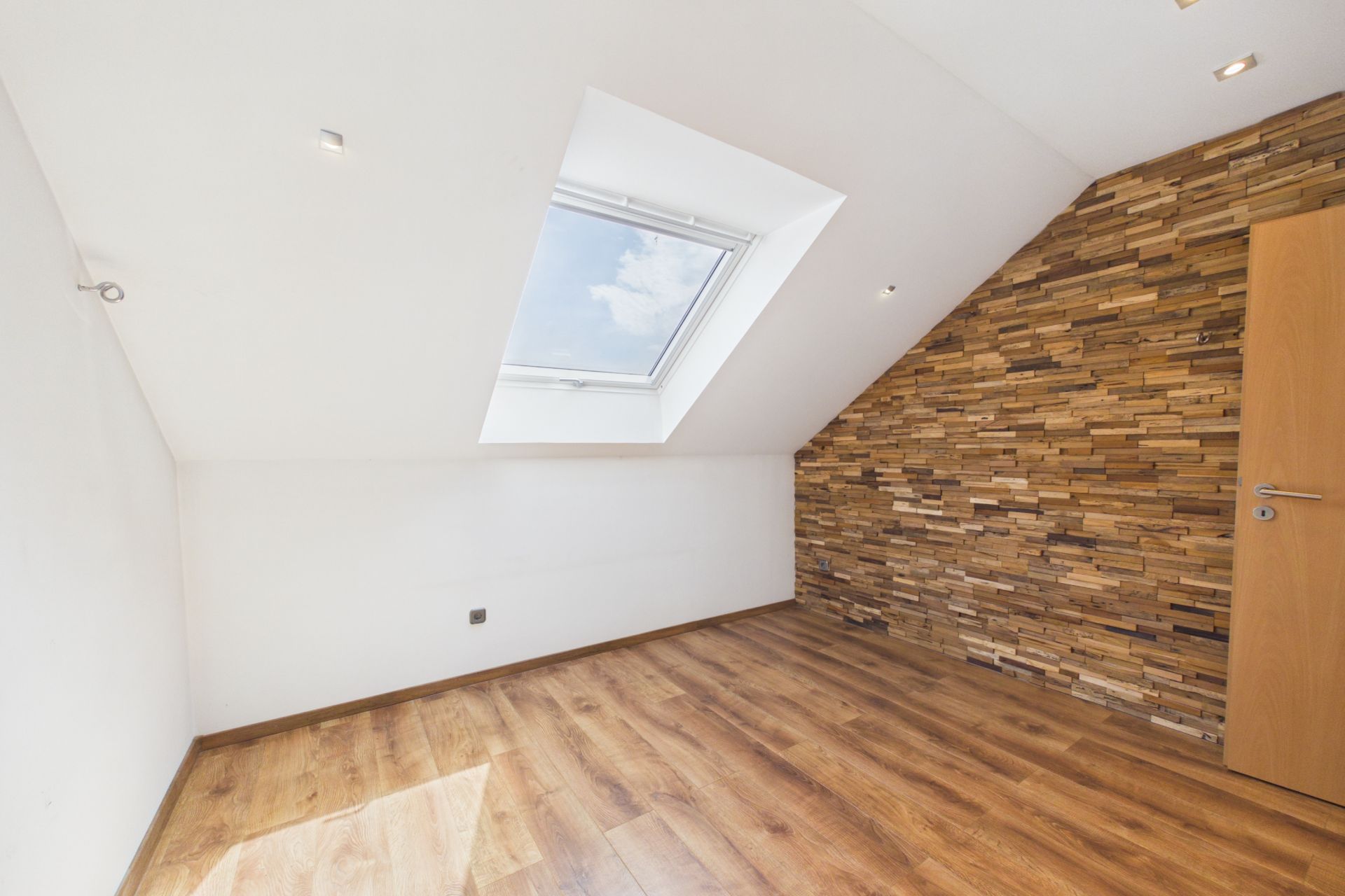 Leerer Raum mit Dachfenster, Holzboden und Wand in Holzoptik.