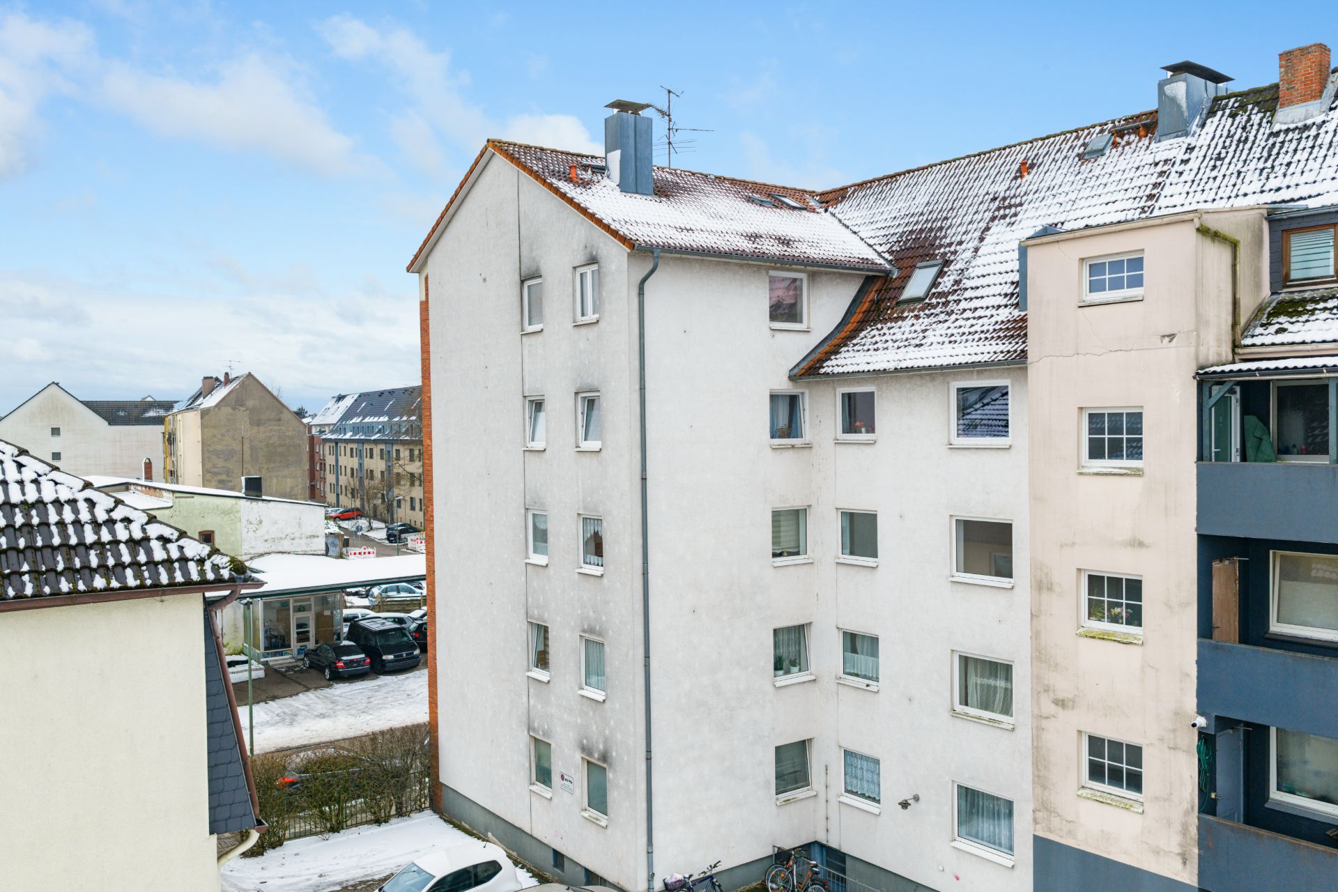 Mehrfamilienhaus mit verschneitem Dach und mehreren Fenstern, im Winter aufgenommen.
