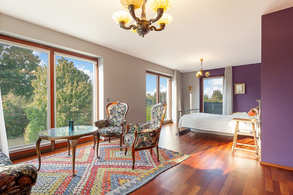 Helles Schlafzimmer mit Holzboden, großen Fenstern, Teppich, Sesseln und Bett.