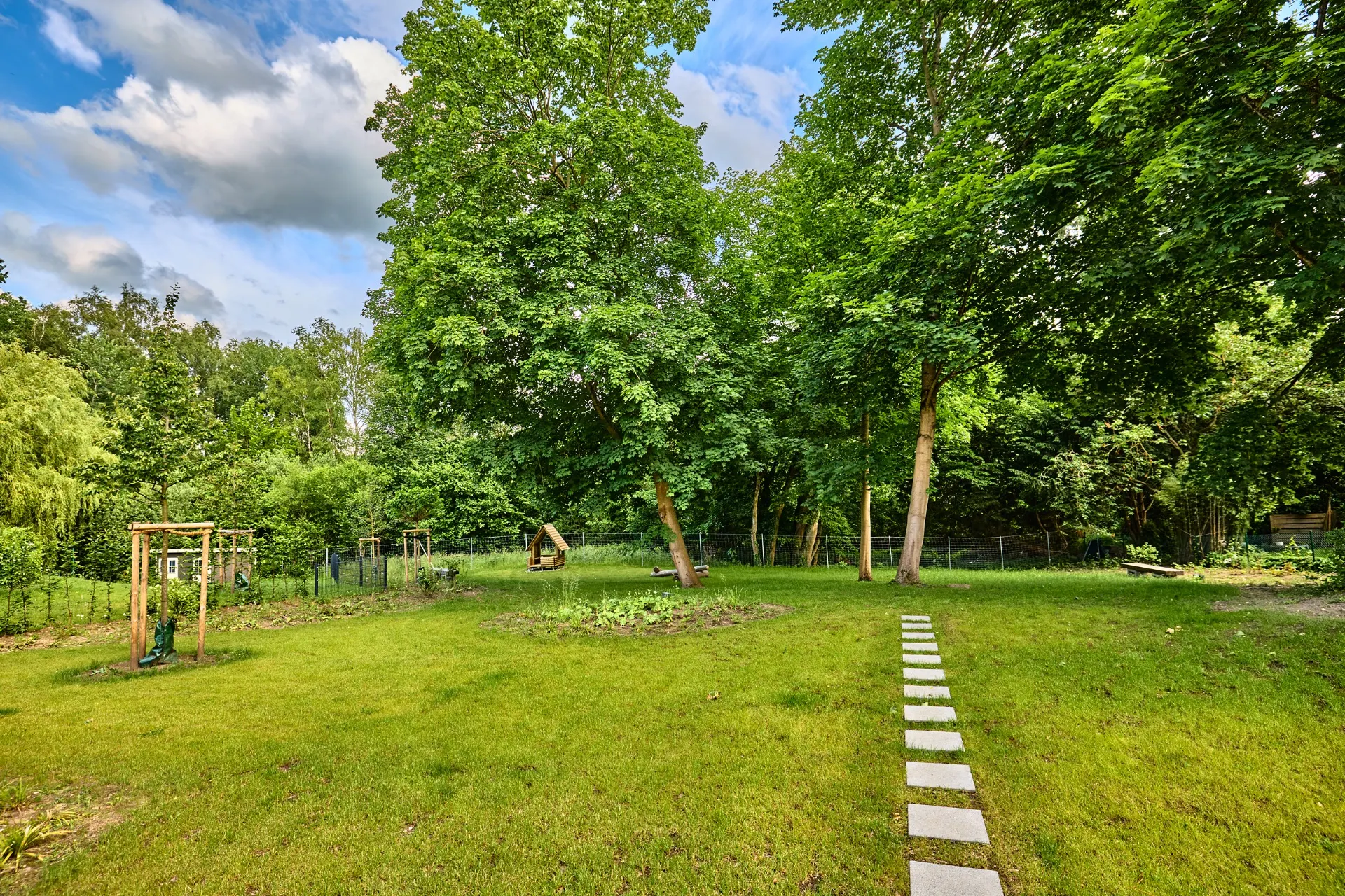 Großer Garten mit grünem Rasen, Bäumen und einem Weg aus Steinplatten.