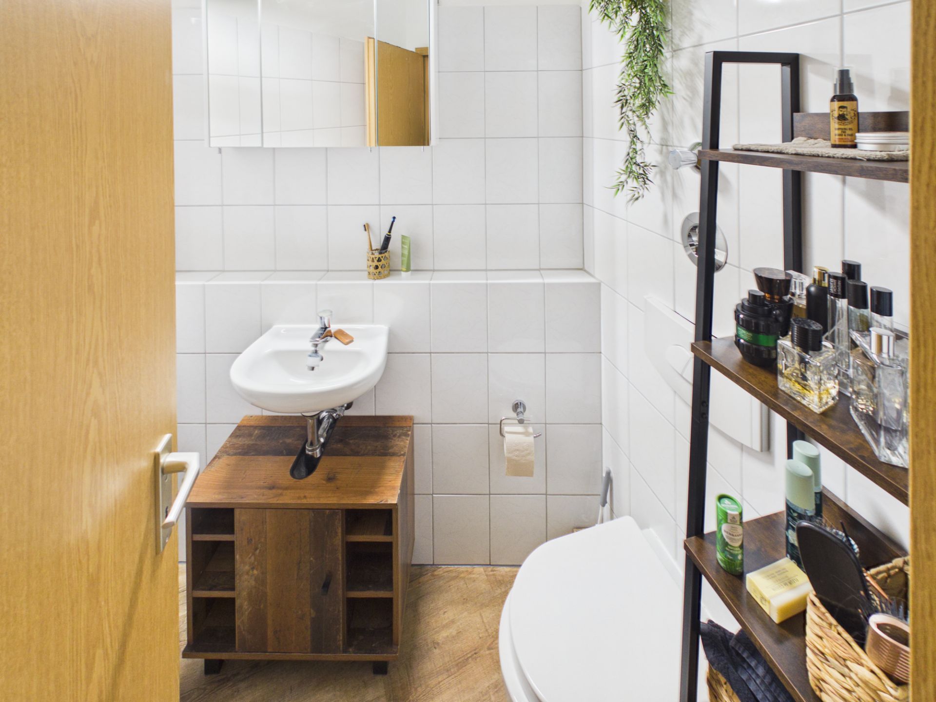 Kleines Badezimmer mit Waschbecken, Regal, WC und weißen Fliesen.