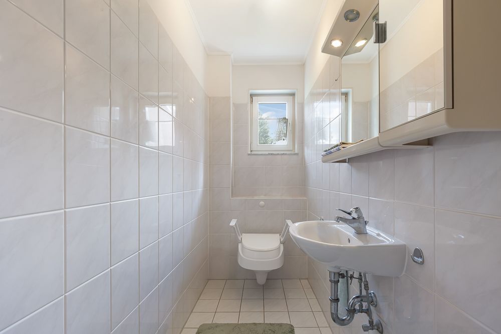 Schmales Badezimmer mit WC, Waschbecken, Spiegelschrank und kleinem Fenster.