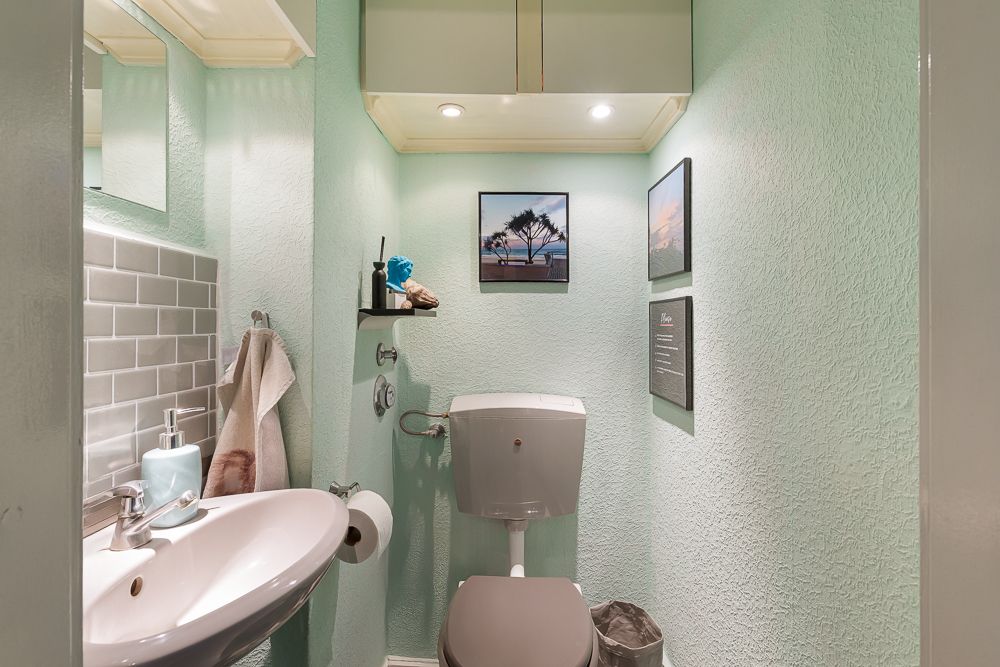 Kleines Badezimmer mit Toilette, Waschbecken, Handtuch, Spiegel und Wandbildern.
