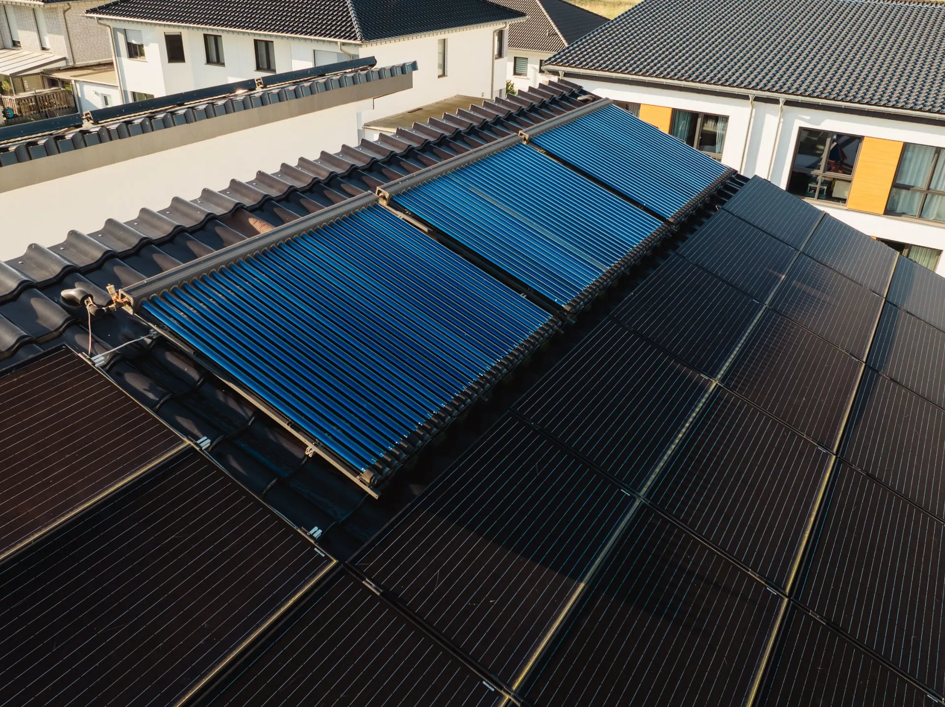 Solarkollektoren und Solarzellen auf einem Hausdach in einem Wohngebiet.