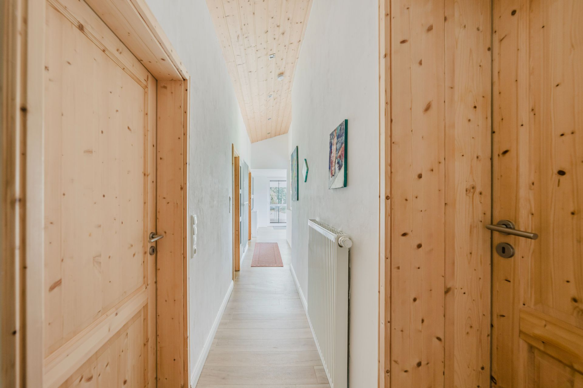 Heller Flur mit Holztüren, weißer Wand, Wandheizung und Bildern an der Wand.