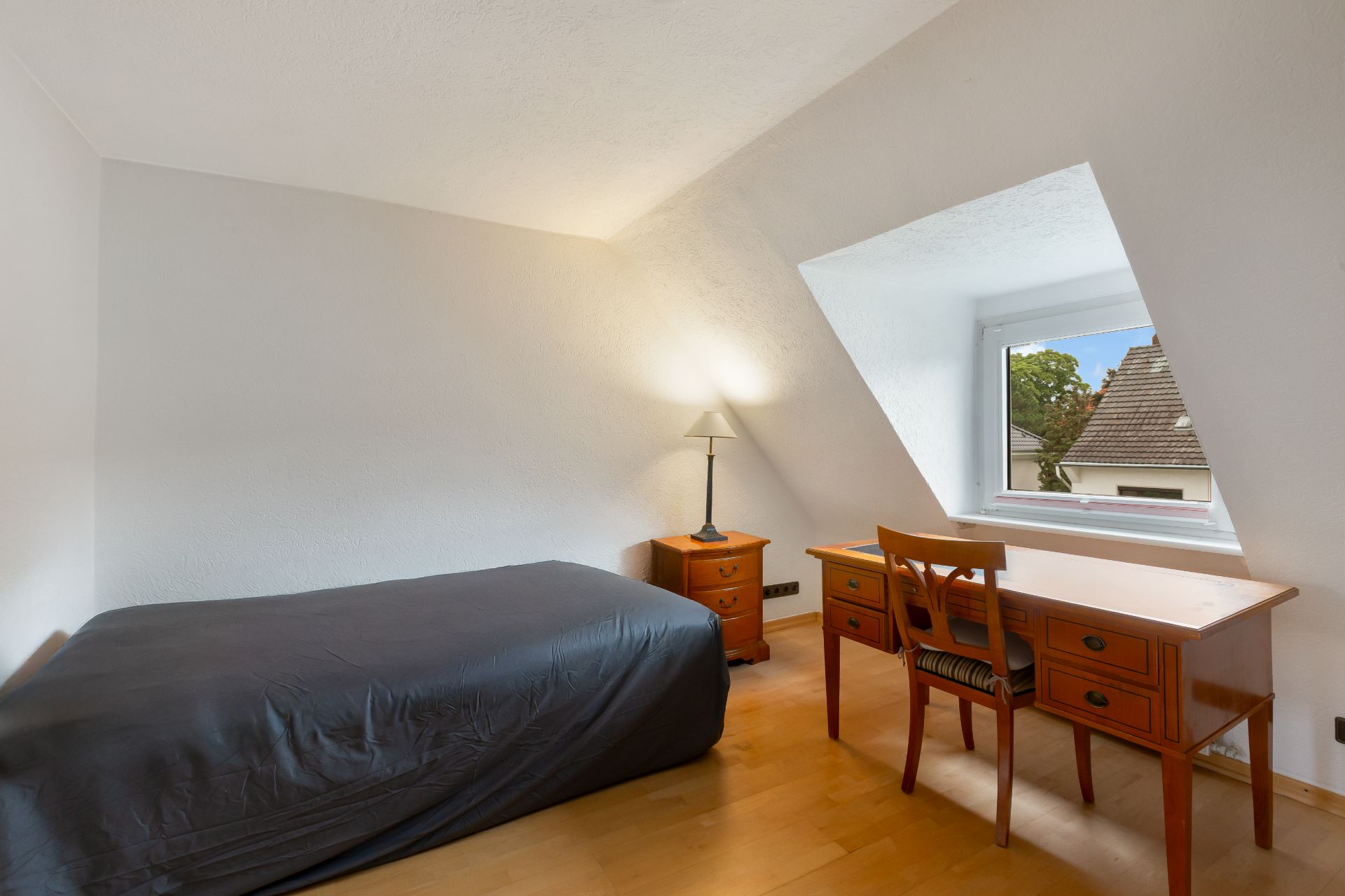 Helles Schlafzimmer mit Einzelbett, Schreibtisch, Stuhl, Nachttisch und Fenster.