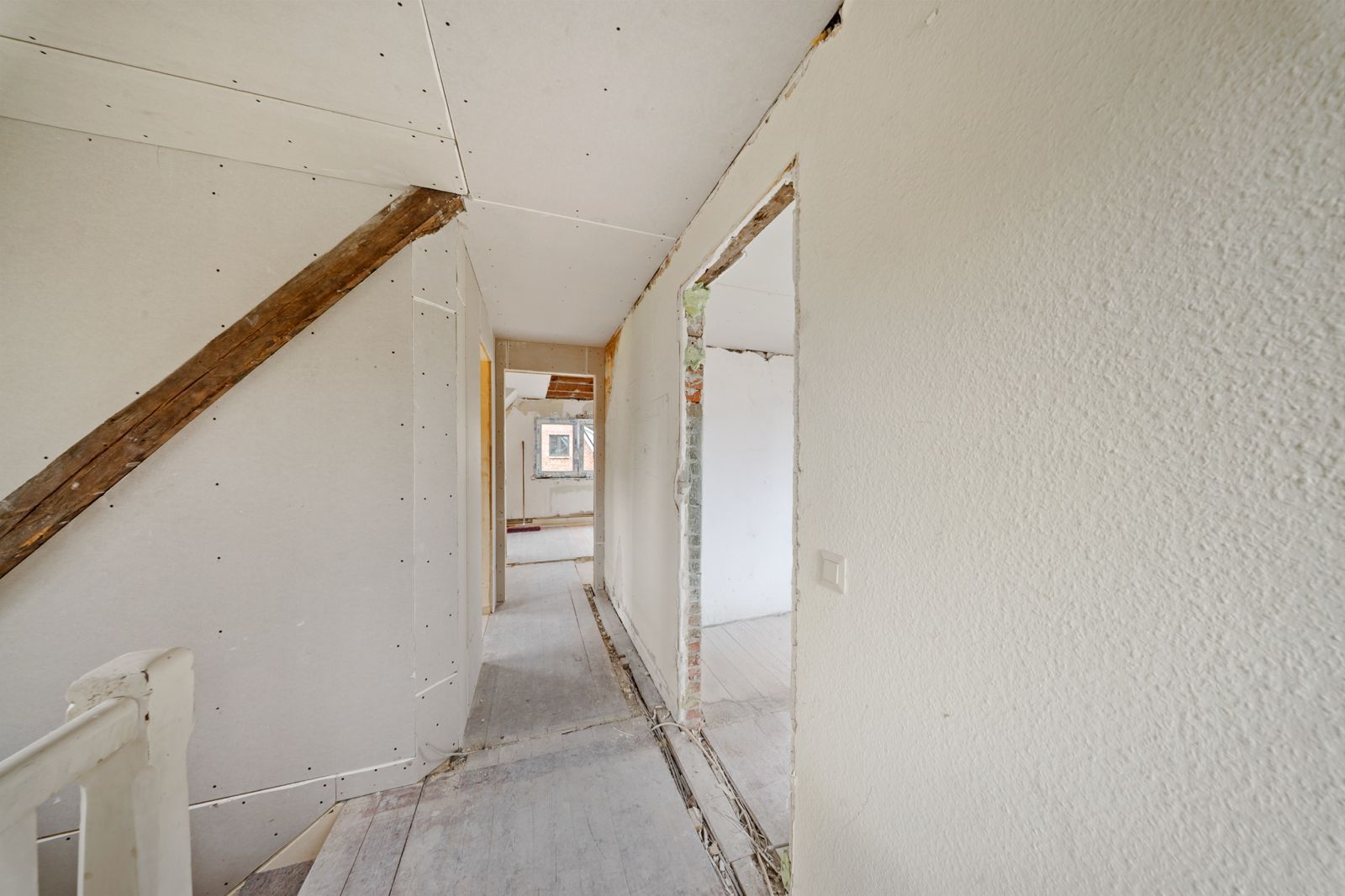 Heller Flur mit sichtbaren Holzbalken und offenen Türrahmen in einem renovierungsbedürftigen Haus.