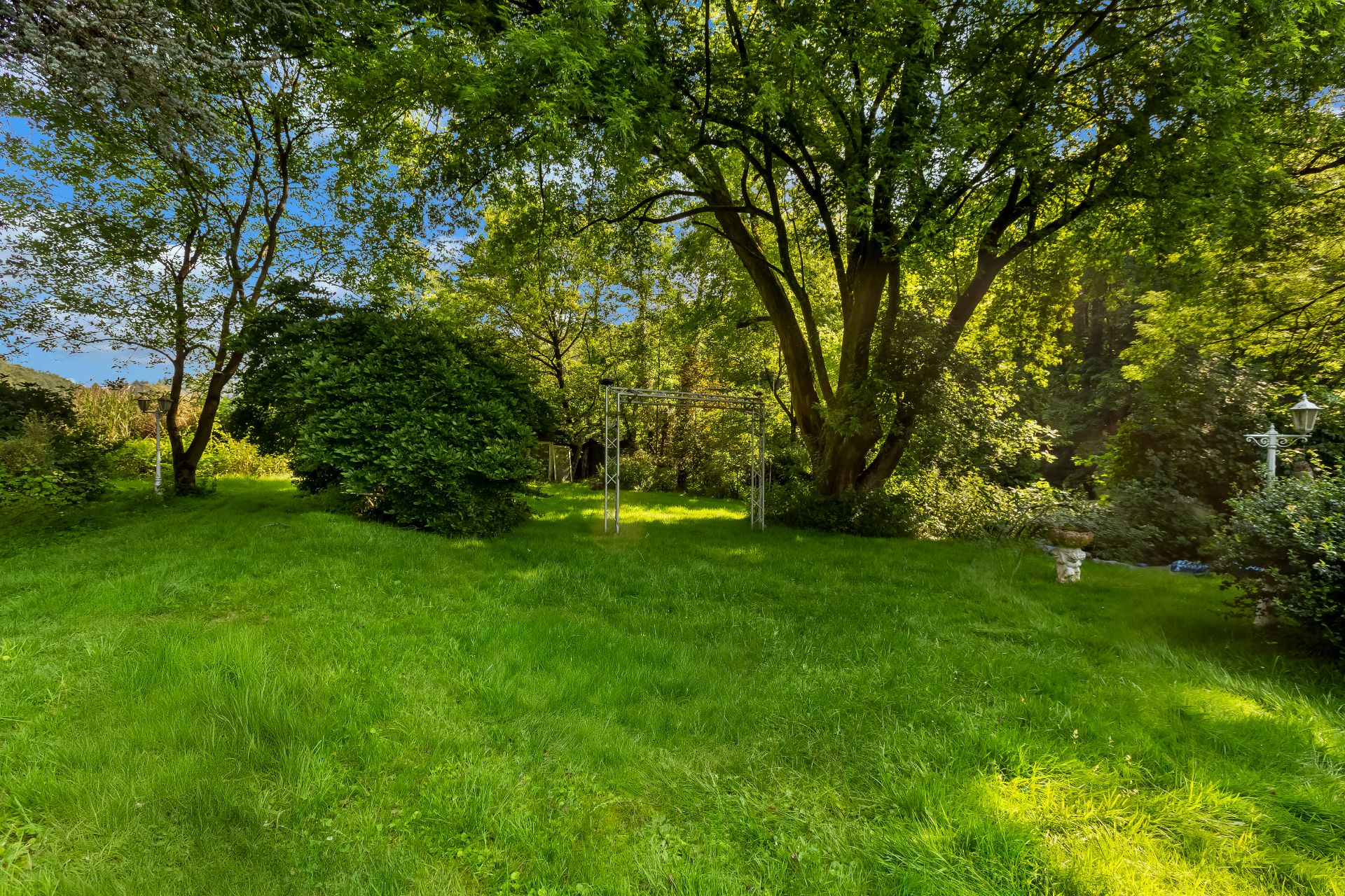 Grüner Garten mit Bäumen, Rasen, einem Metallgestell und einer weißen Gartenlampe.