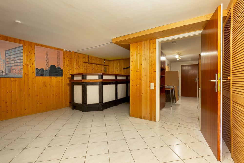 Kellerraum mit gefliesten Böden, Holzvertäfelung und offener Tür zum Flur.