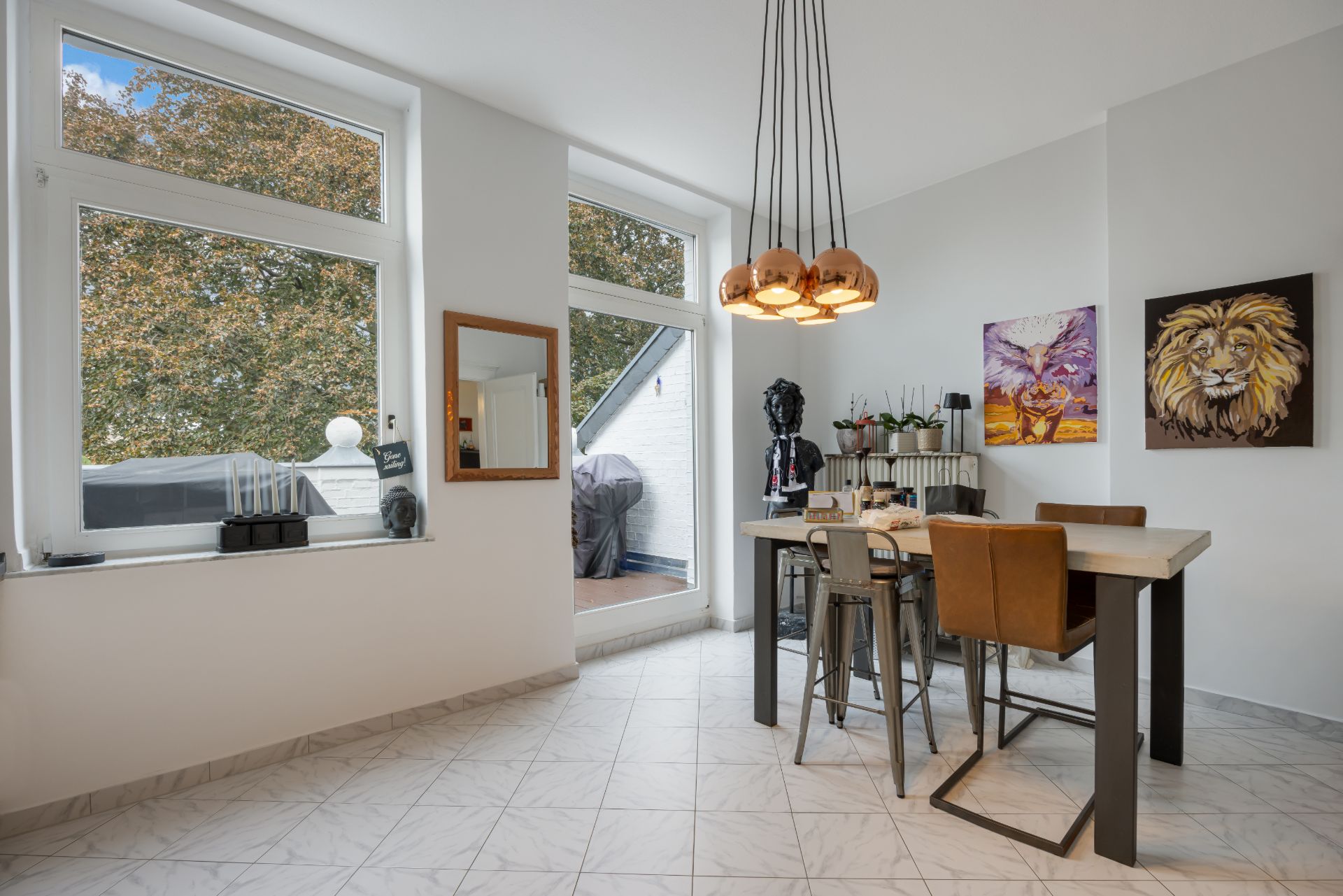 Essbereich mit Tisch, vier Stühlen, Gemälden an der Wand und großen Fenstern mit Blick nach draußen.