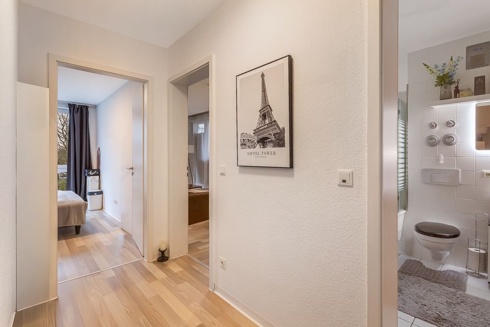 Heller Flur mit Holzfußboden, Zugang zu Schlafzimmer und Bad, Bild mit Eiffelturm an der Wand.