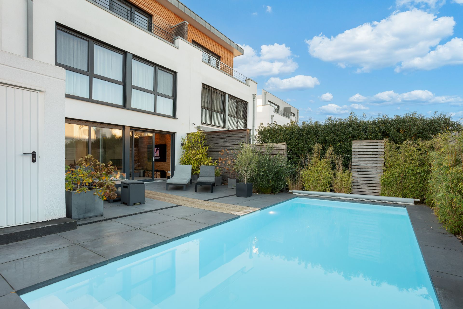 Moderne Terrasse mit Pool, Liegestühlen und Pflanzen vor einem Wohnhaus.