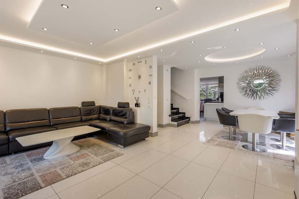 Modernes Wohnzimmer mit schwarzem Ecksofa, Couchtisch, Esstisch und großer Wanduhr.