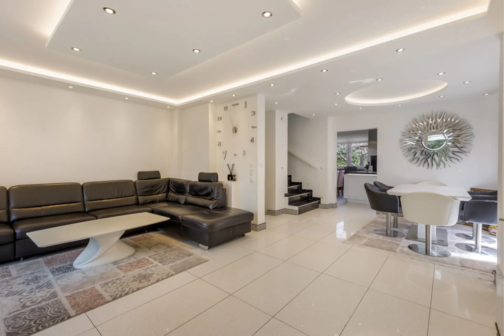 Modernes Wohnzimmer mit schwarzem Ecksofa, Couchtisch, Esstisch und großer Wanduhr.