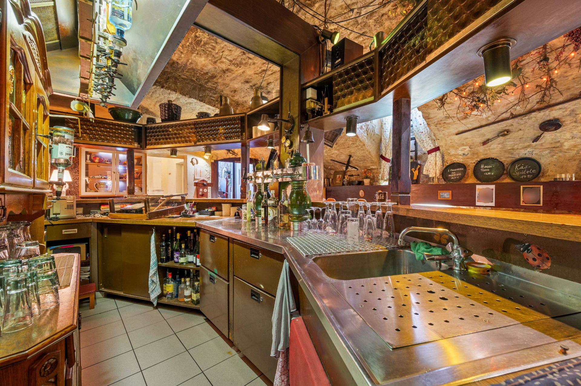 Kleine Hausbar mit Theke, Küchenspüle, Gläsern, Flaschen und Regalen unter einem Gewölbedeckenraum.