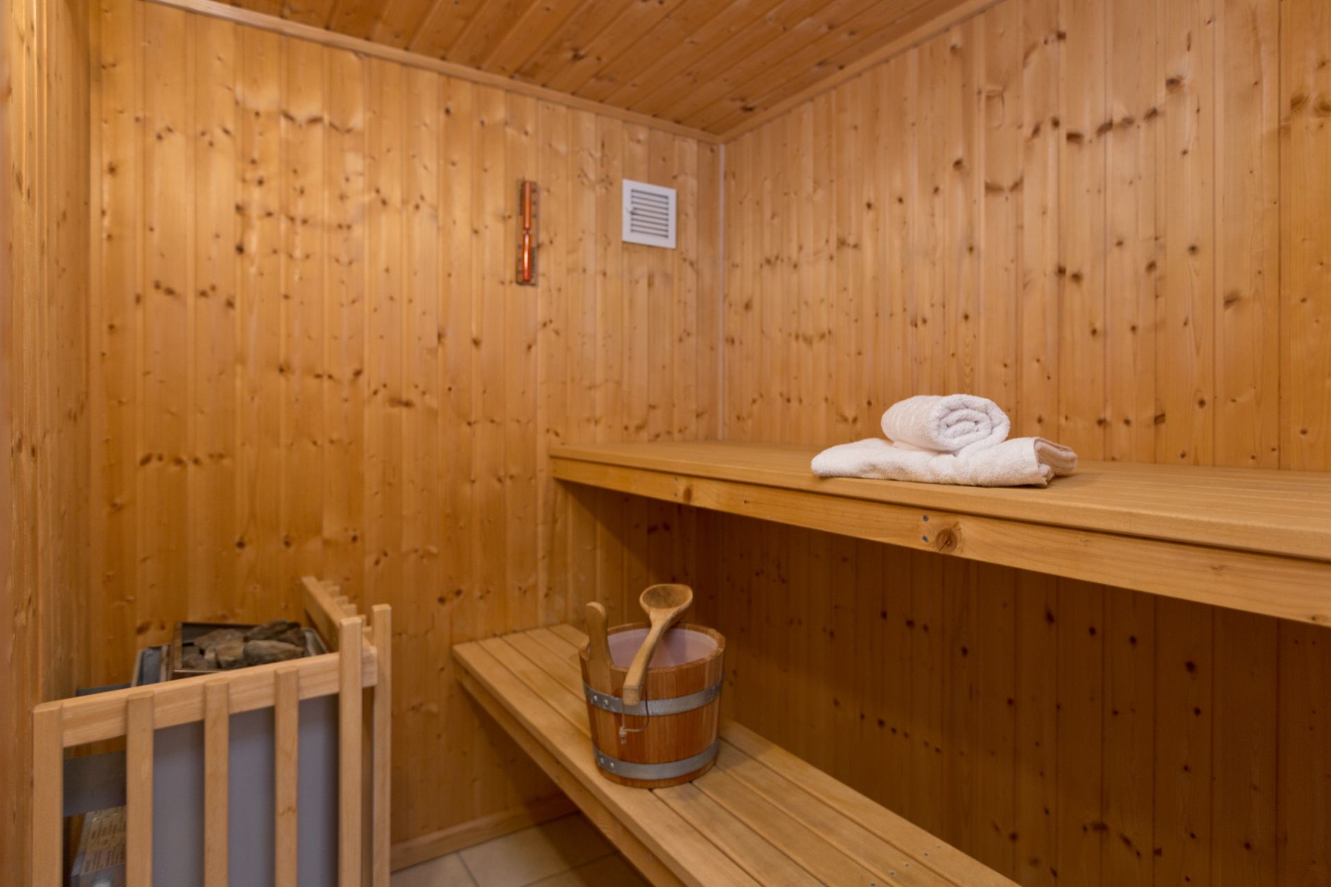 Holzsauna mit Bänken, Eimer, Kelle und Handtüchern auf der oberen Bank.