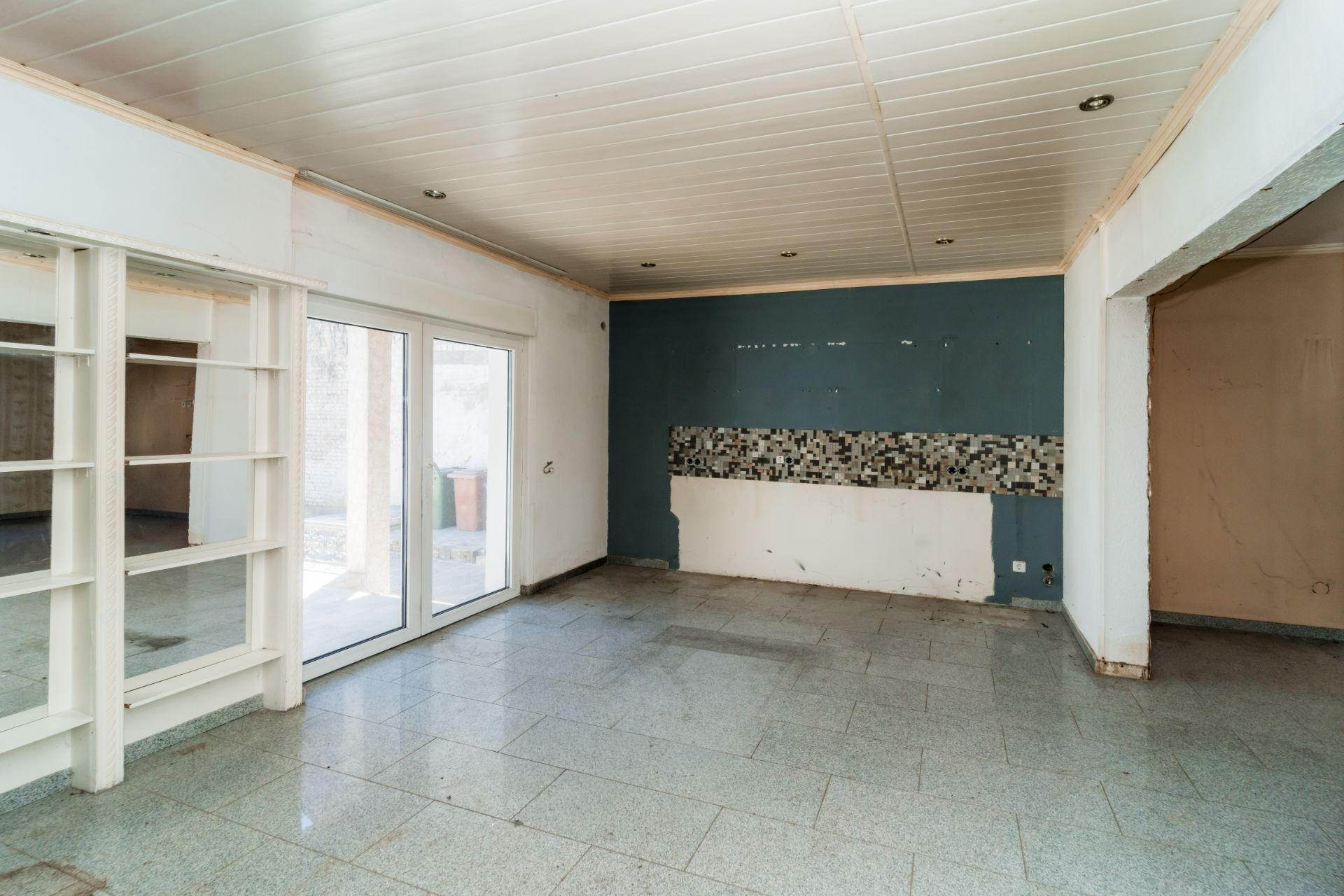 Leerer Raum mit Fliesenboden, Schiebetür, Regalwand und teils gefliester Wand.