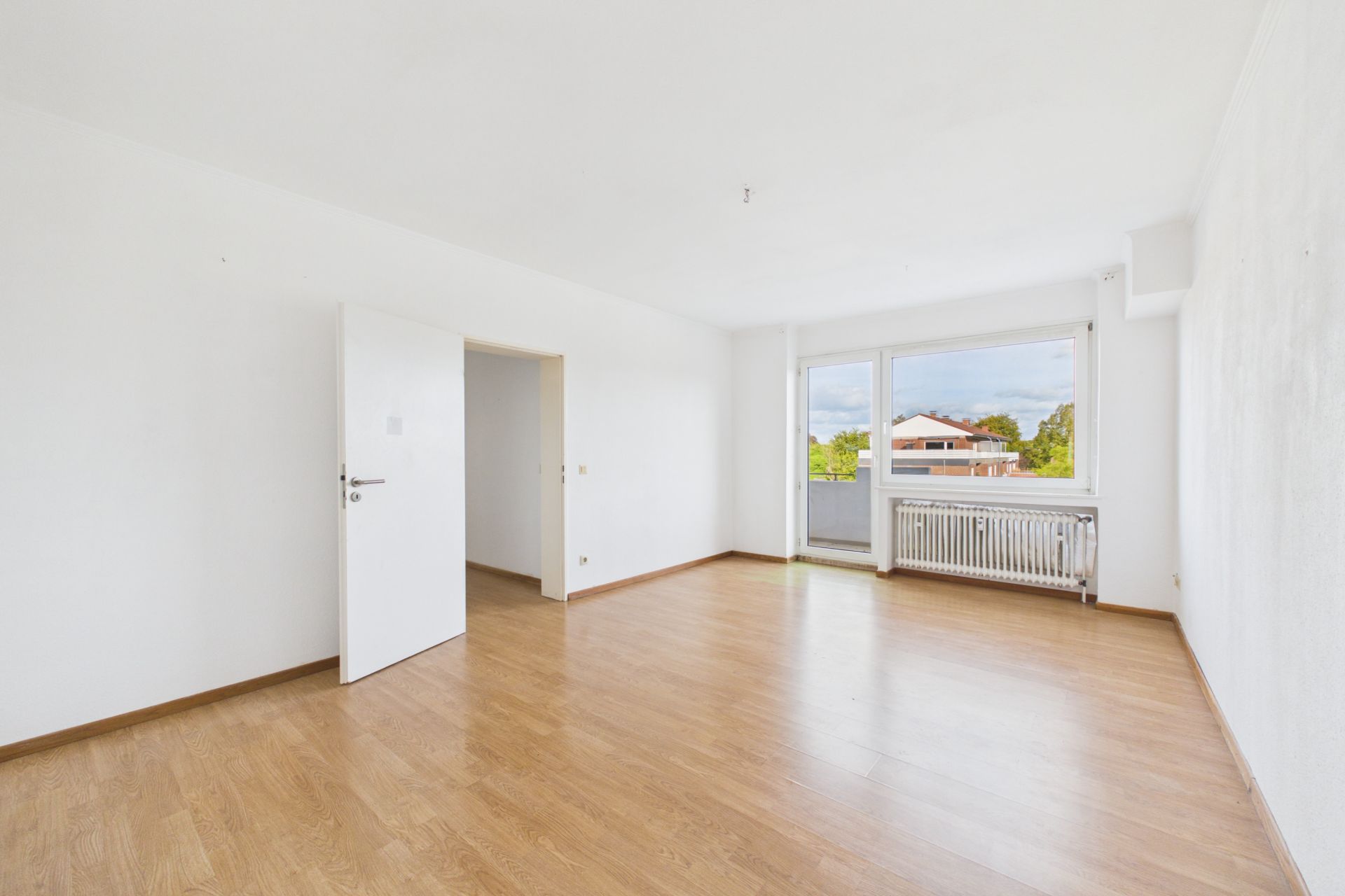 Helles, leeres Zimmer mit Parkettboden, offenem Fenster und Tür.
