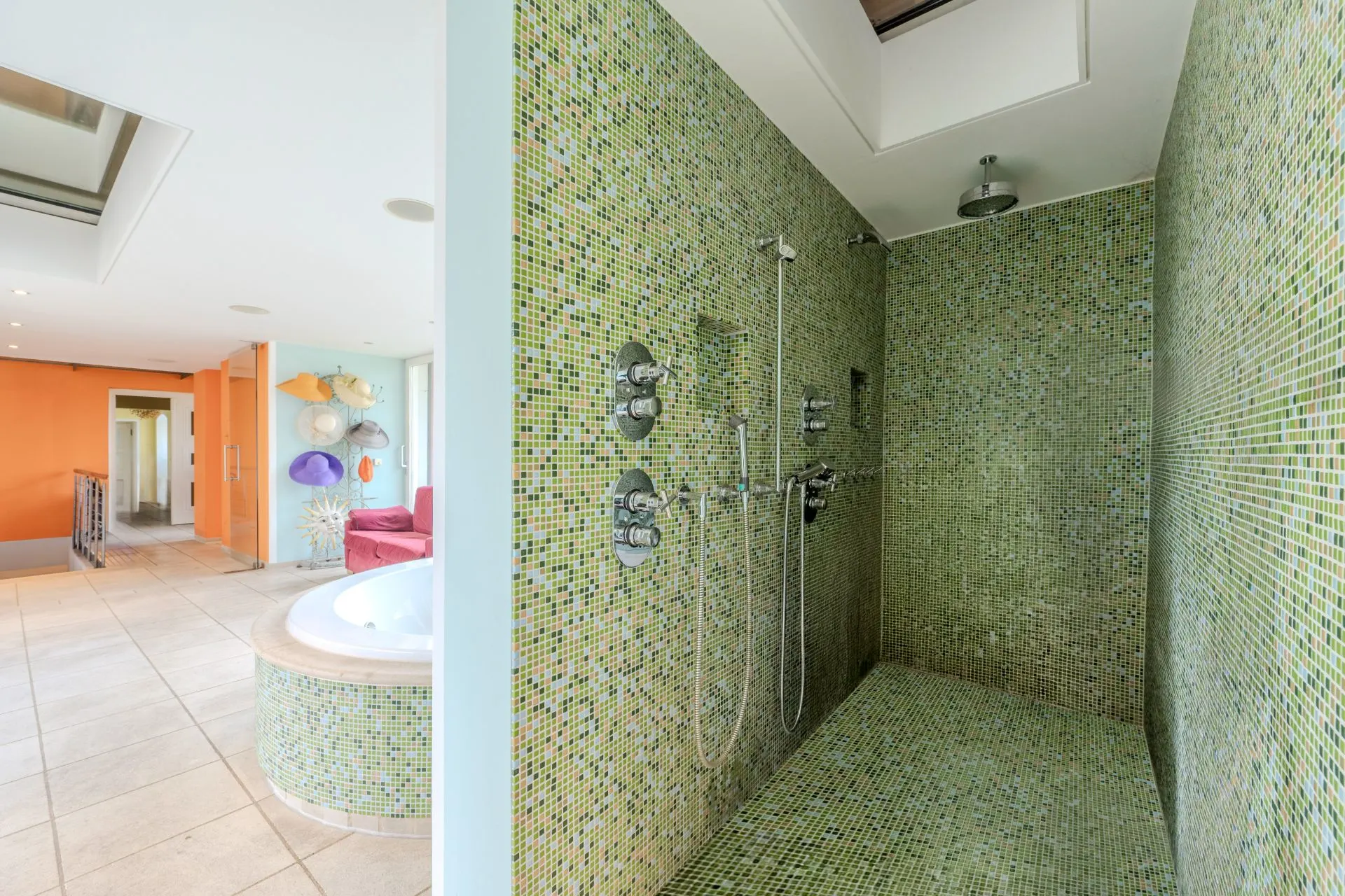 Große Dusche mit grünen Mosaikfliesen, daneben ein runder Whirlpool in einem hellen Raum.