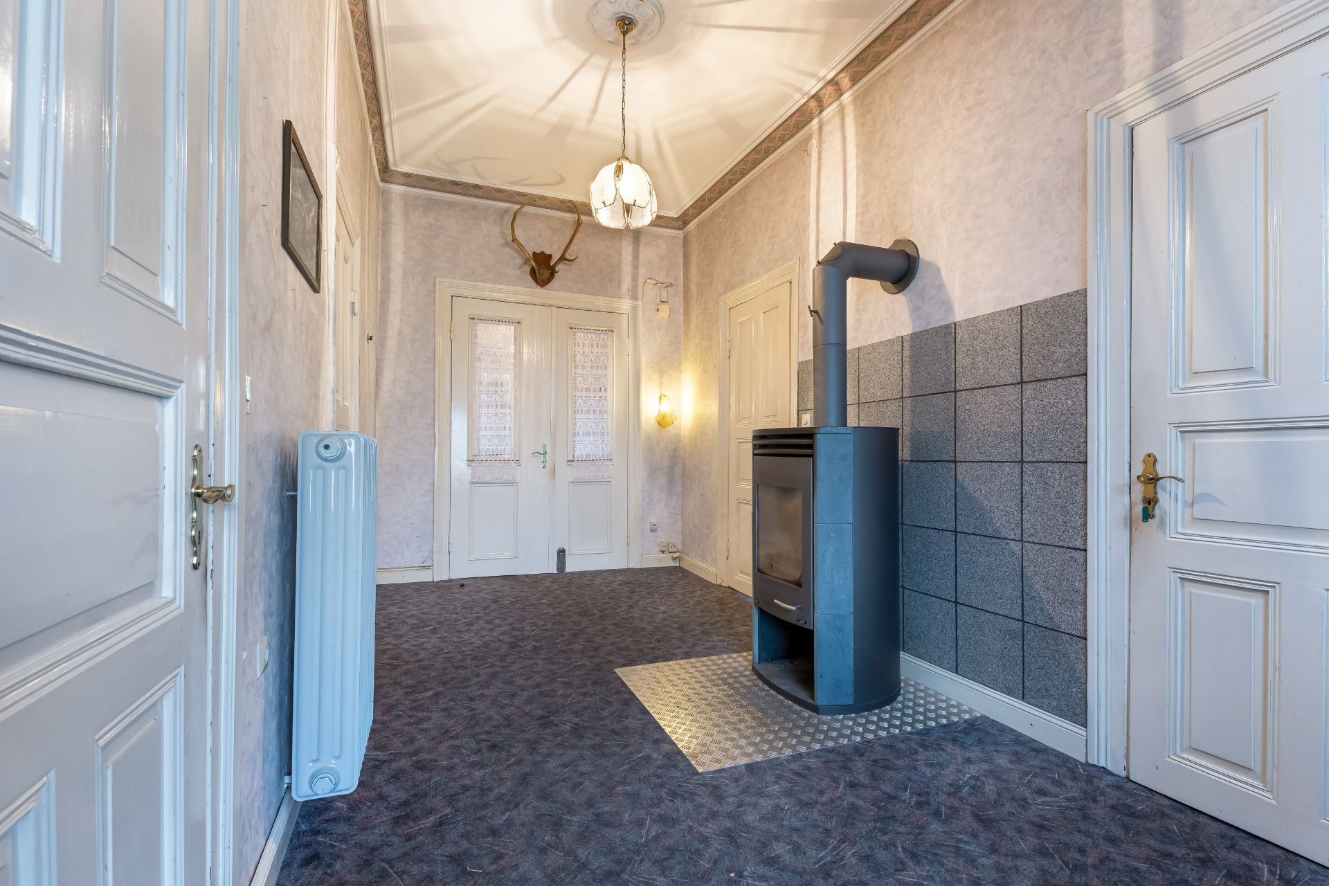 Heller Flur mit Kaminofen, Heizkörper, Doppeltür und Geweih an der Wand.