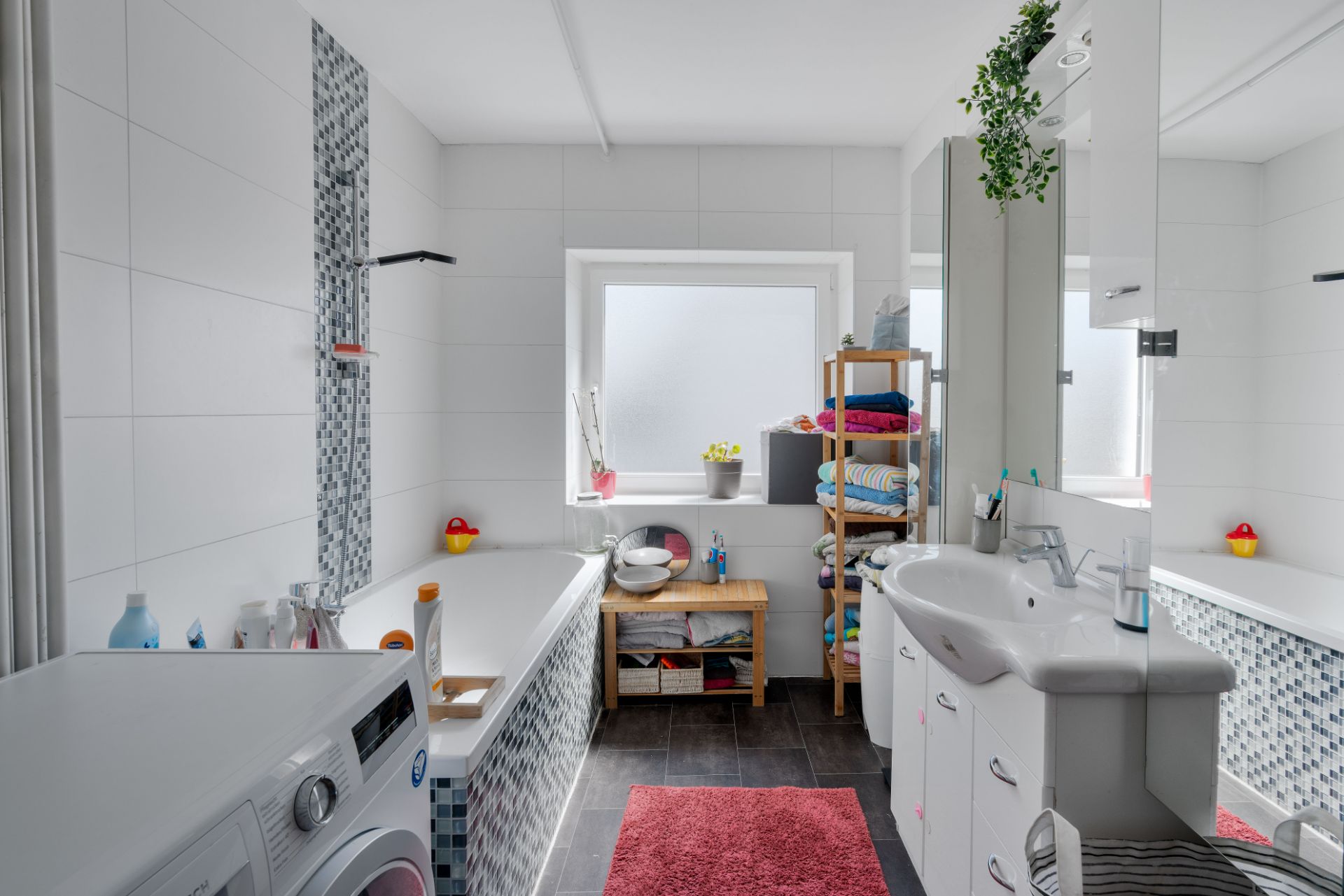Modernes Badezimmer mit Badewanne, Waschbecken, Waschmaschine und Regal mit Handtüchern.