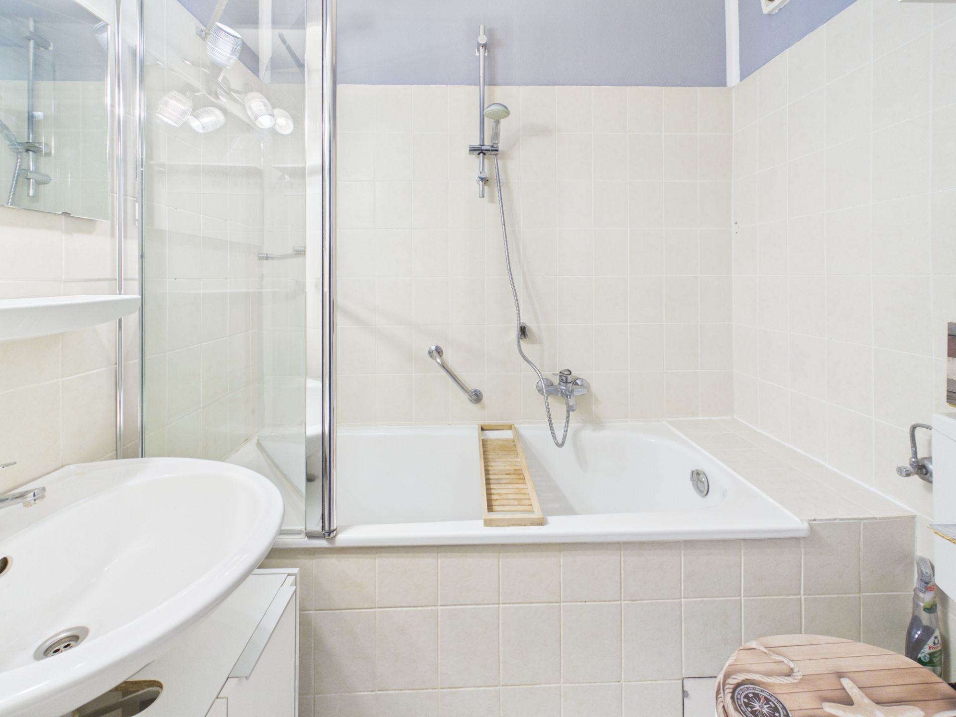 Helles Badezimmer mit Badewanne, Duschwand, Waschbecken und hellen Fliesen.