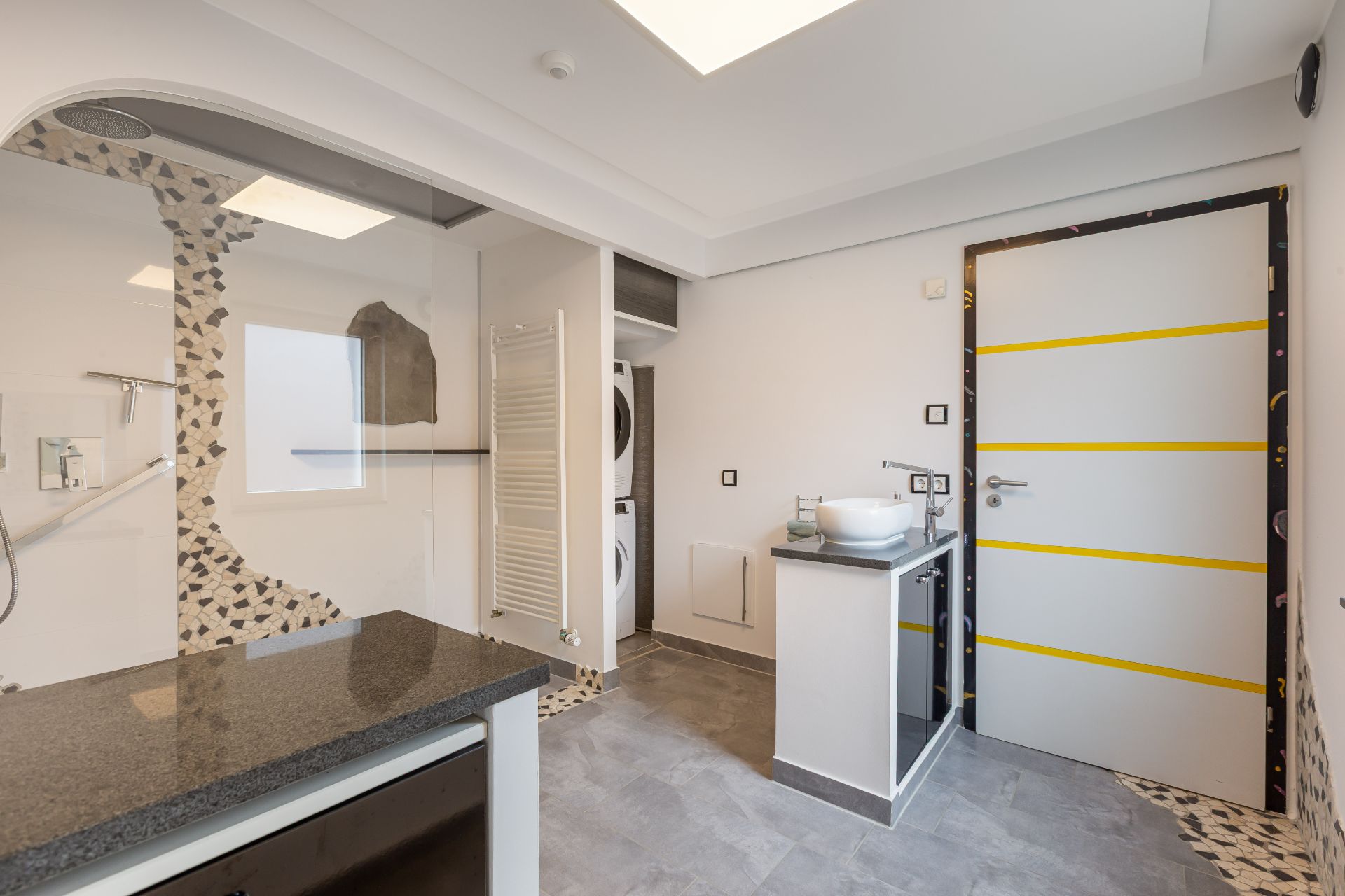Modernes Badezimmer mit Dusche, Waschmaschine, Waschbecken und gemustertem Boden.